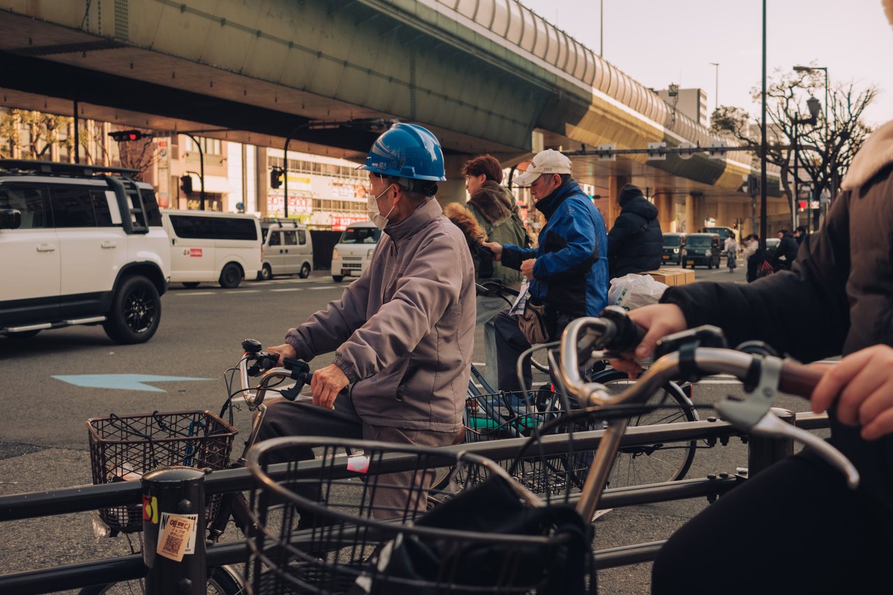 Cyclists waiting under an elevated expressway by day, Osaka