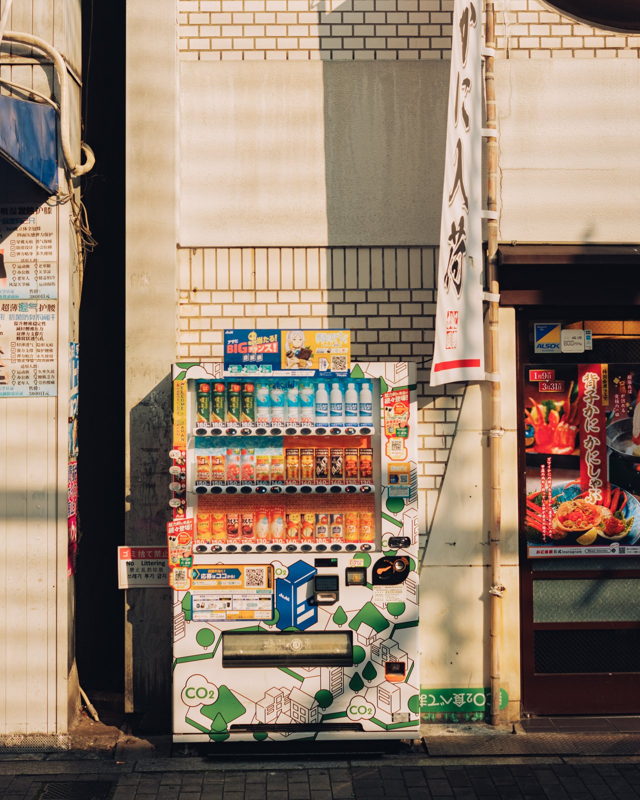 A bank of vending machines against a tiled wall beside a shop, Osaka