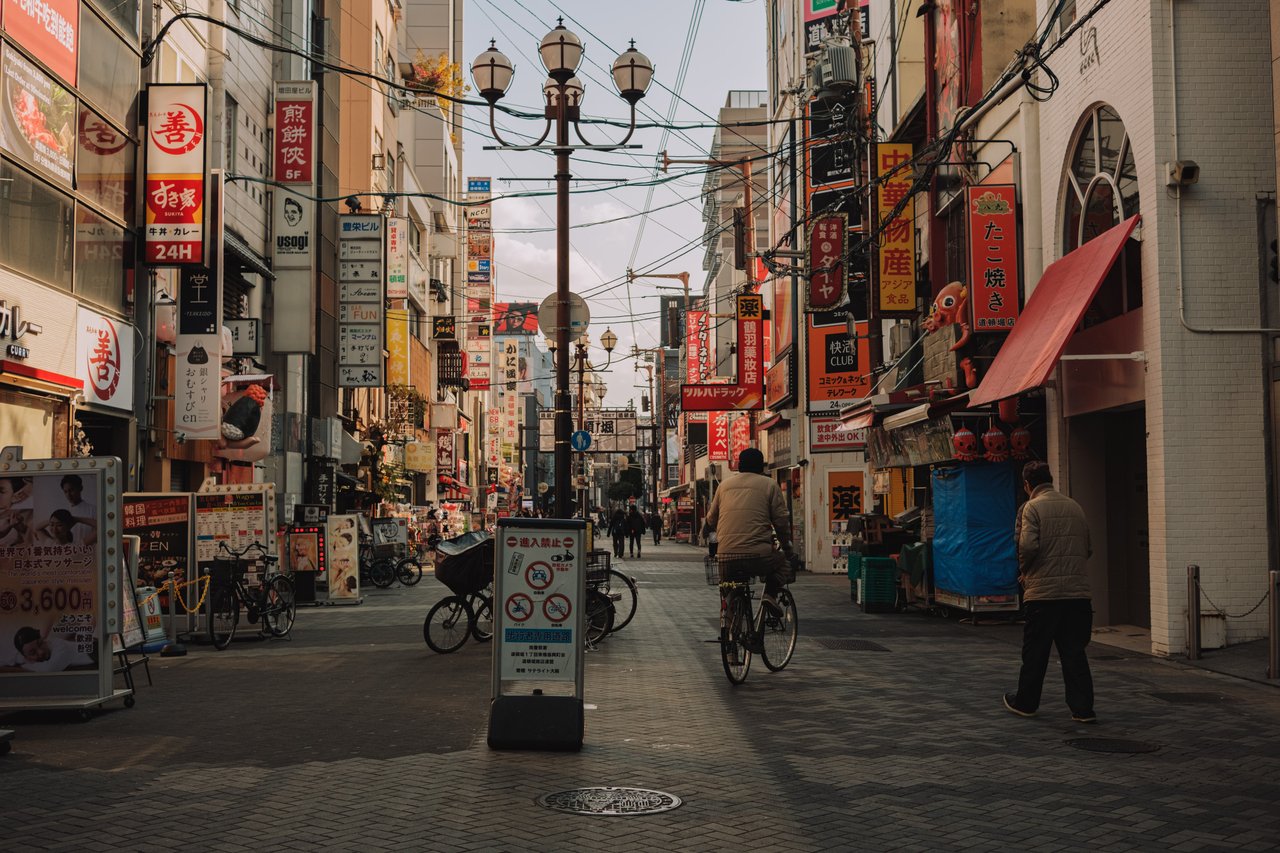 A lamplit shopping street with hanging signage and a cyclist, Shinsekai, Osaka