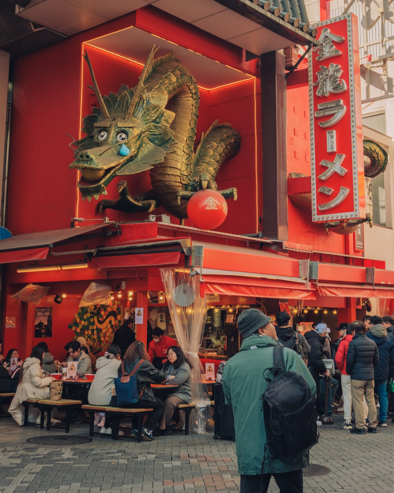 The Kinryu Ramen dragon sign glowing red over diners at outdoor tables, Dotonbori, Osaka