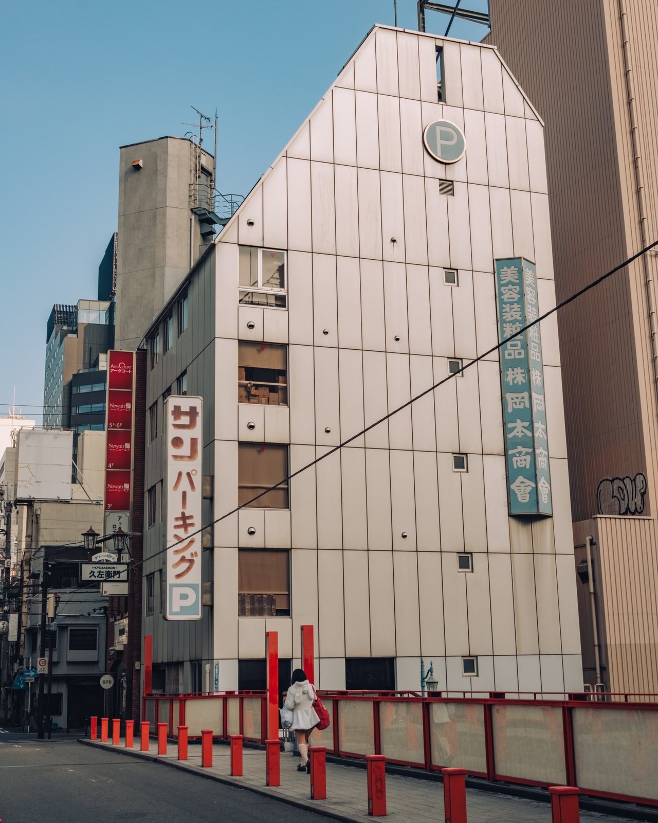 A modern white building with a Sun Parking sign and red bollards, Osaka