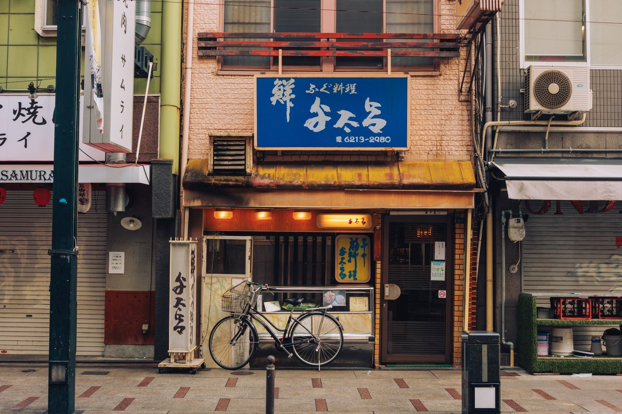 A corner restaurant with a blue sign and a parked bicycle, Osaka