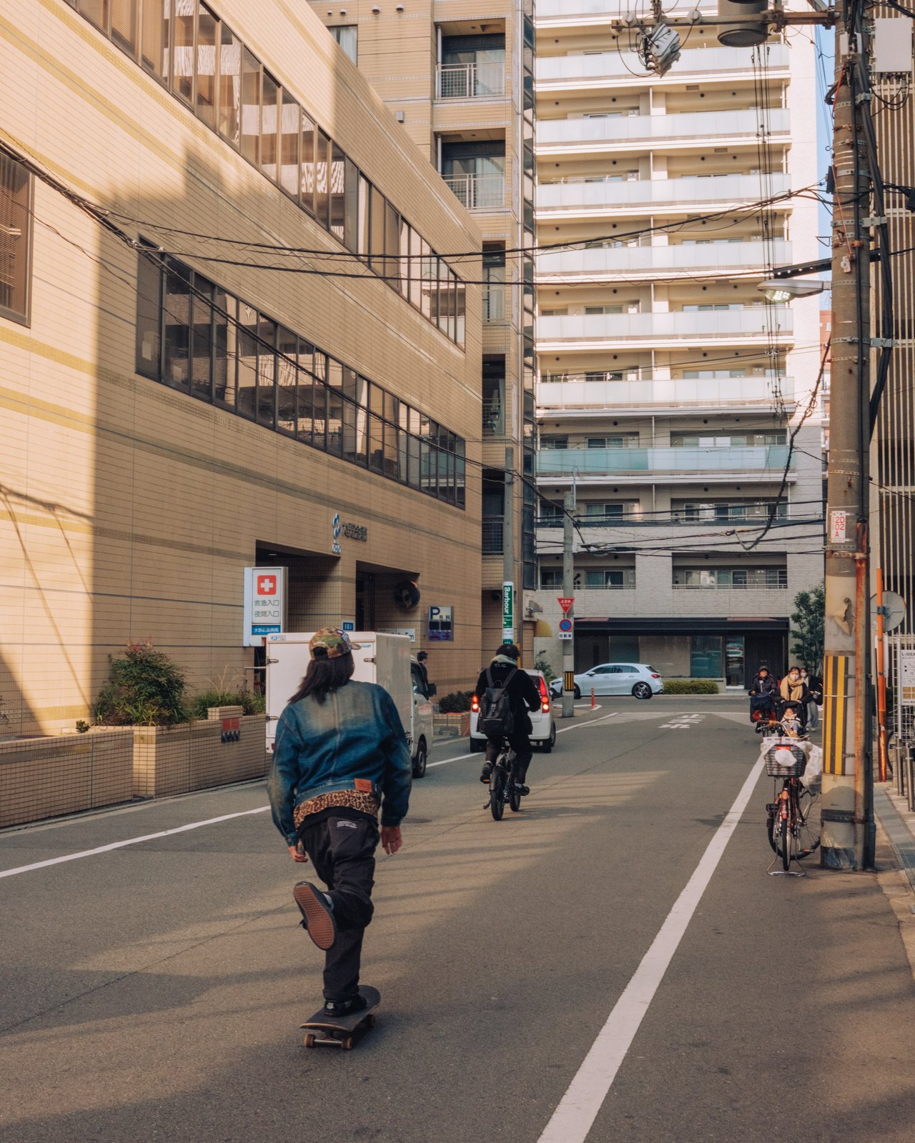A skateboarder rolling down a sunlit street between apartment blocks, Osaka