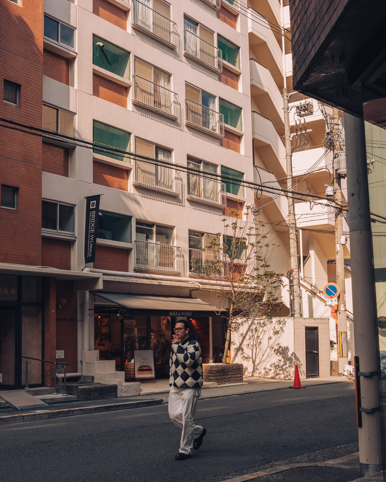 A man in a checkered sweater crossing a street below apartment blocks, Osaka