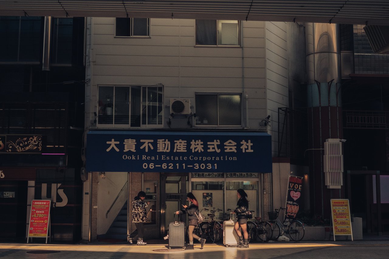 A corner by the Ooki real-estate office, people waiting in the sun, Osaka