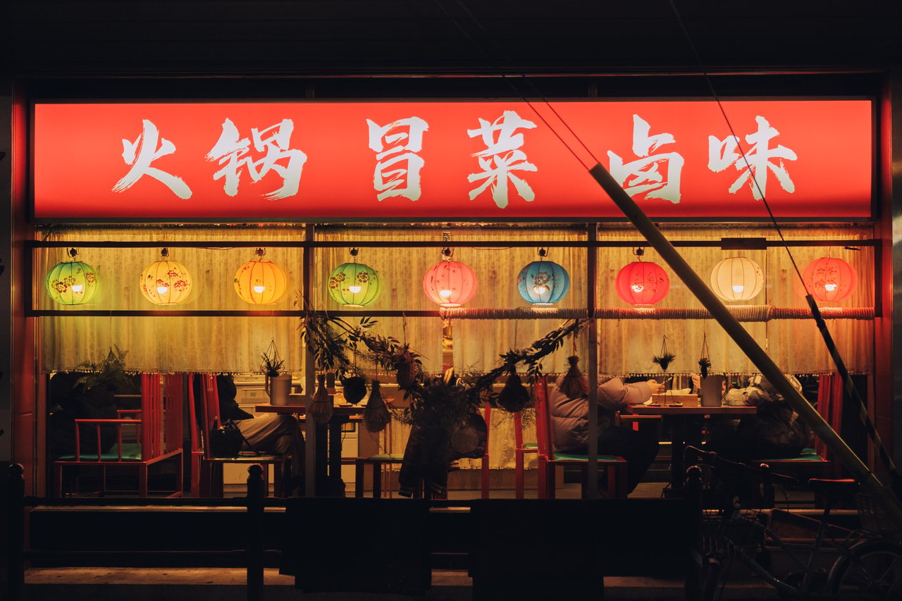 A red-fronted hotpot restaurant window glowing with paper lanterns, Osaka