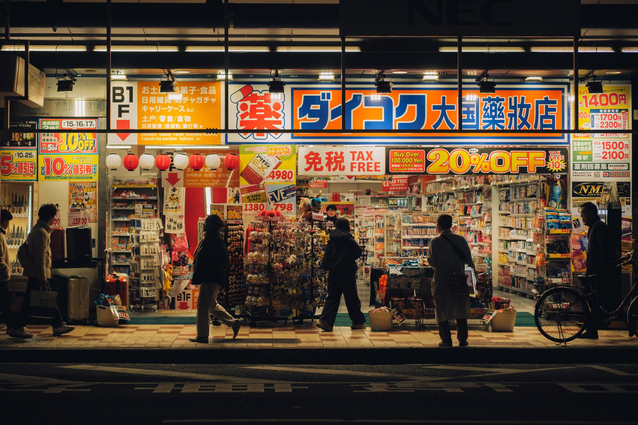 A Daikoku drugstore front at night with tax-free signs and shoppers, Osaka