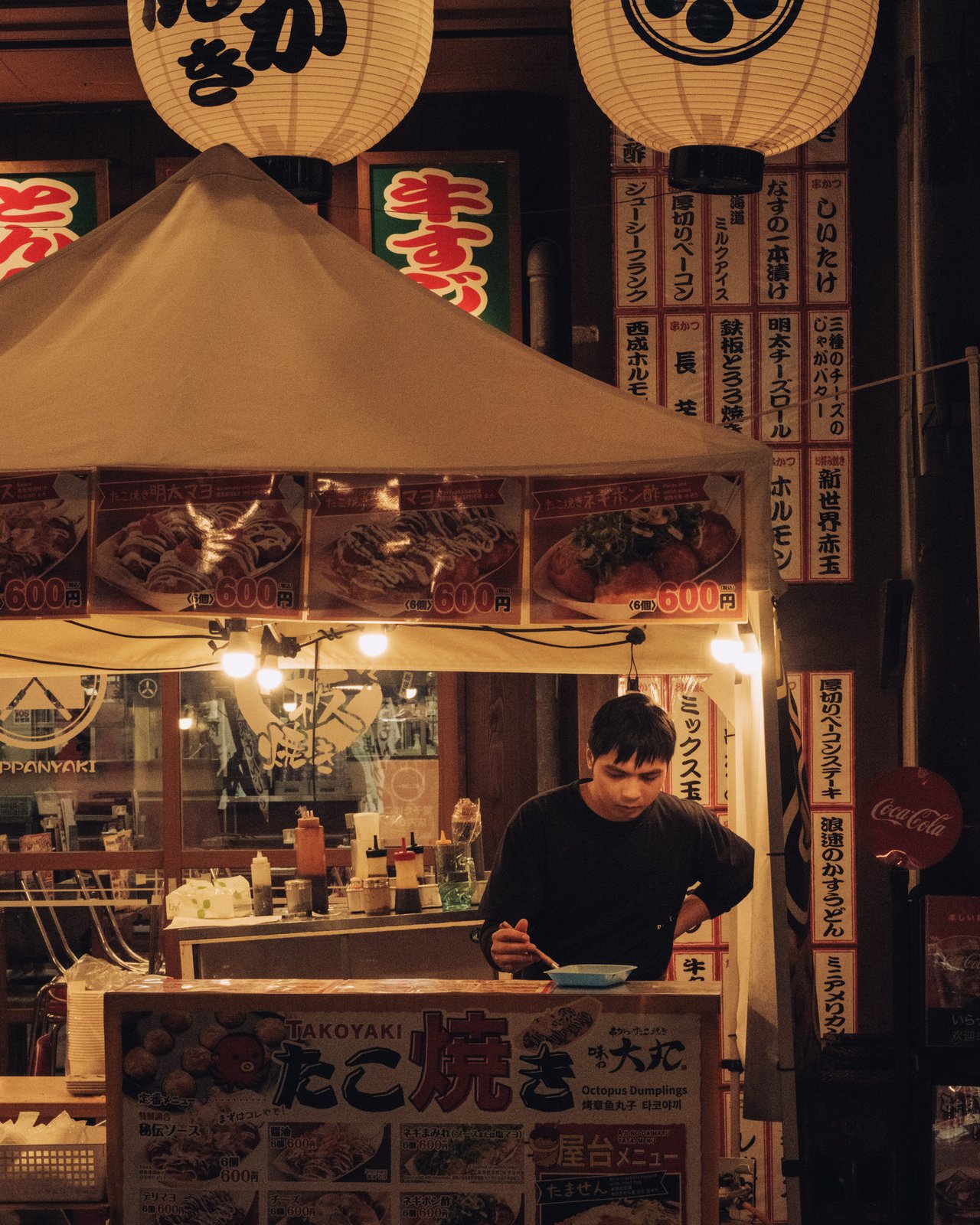 A takoyaki street stall at night, a cook at work under red lanterns, Osaka