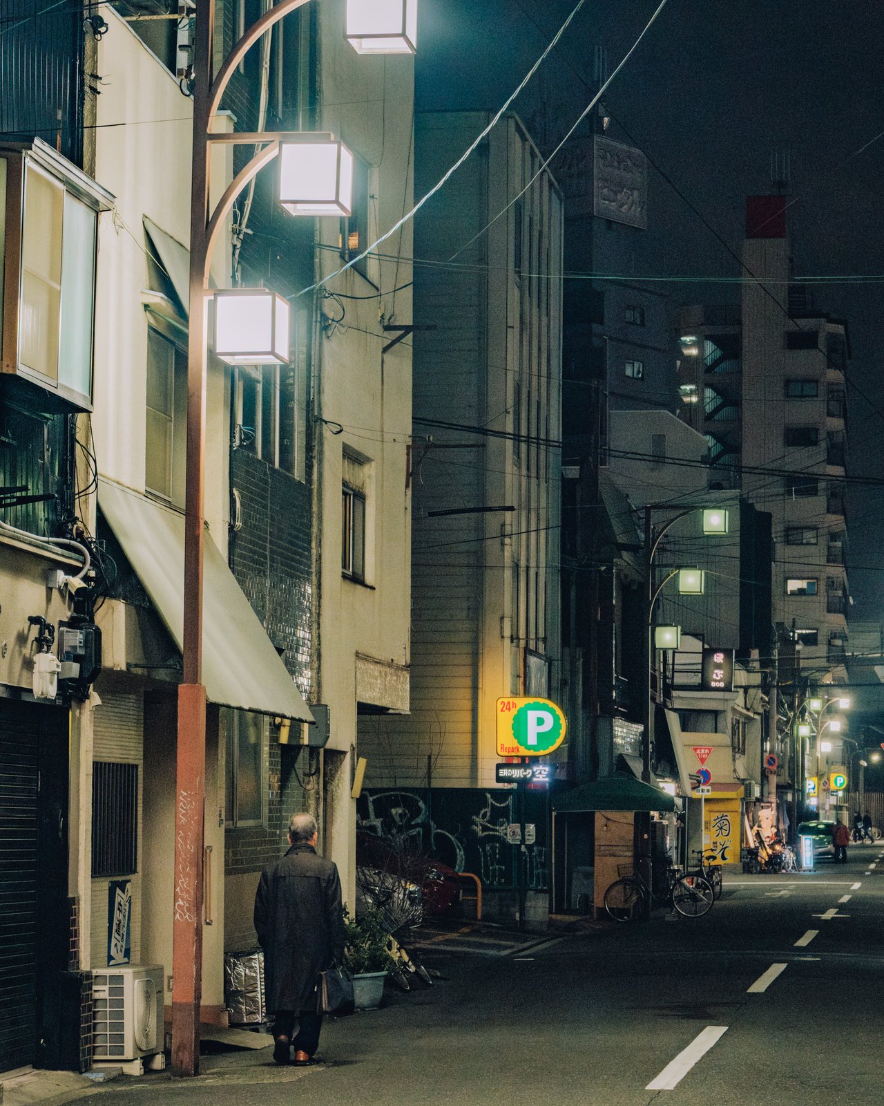 A quiet residential night street with lanterns and a lone figure, Osaka