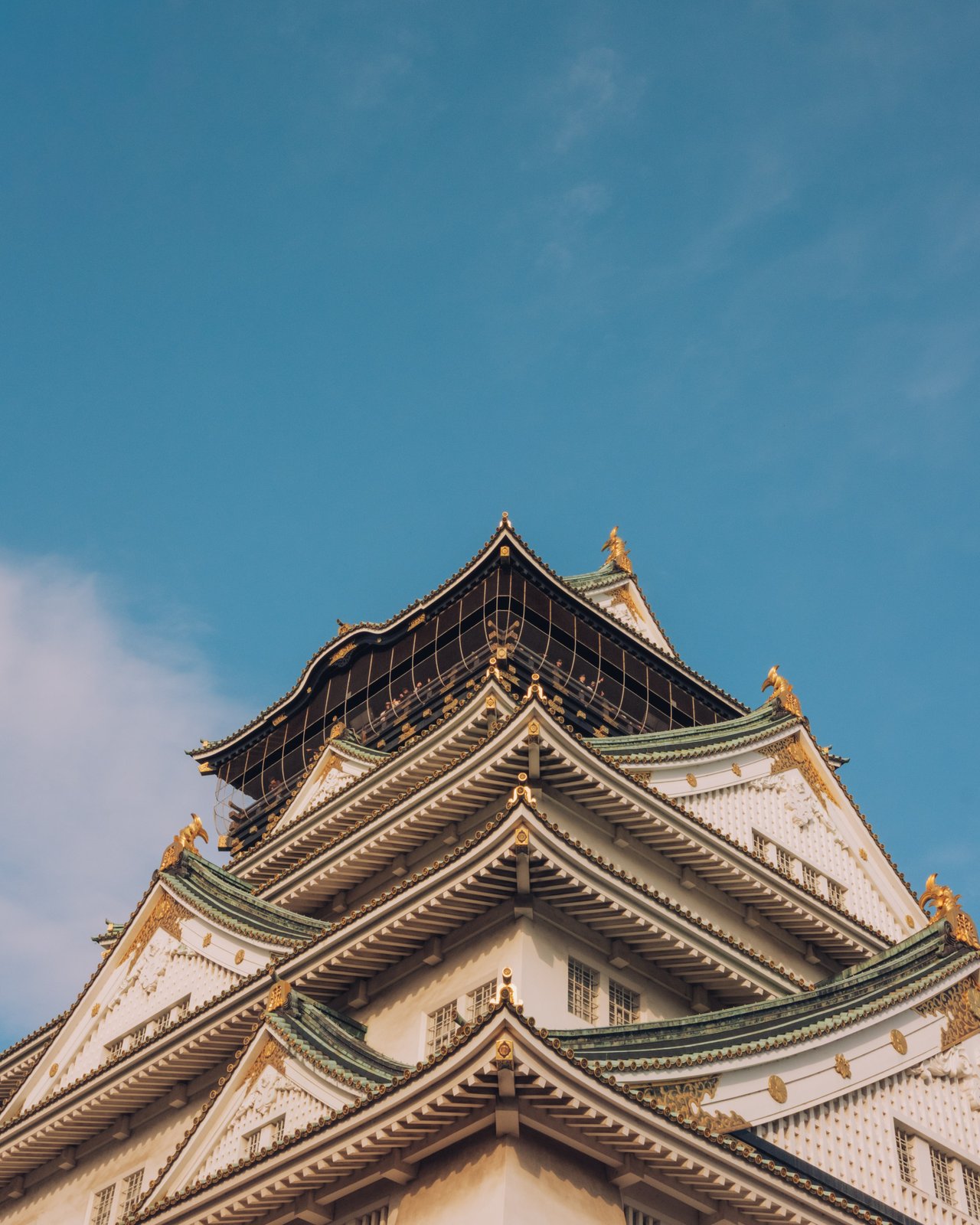 The roofline of Osaka Castle's keep with gold ornaments against a blue sky