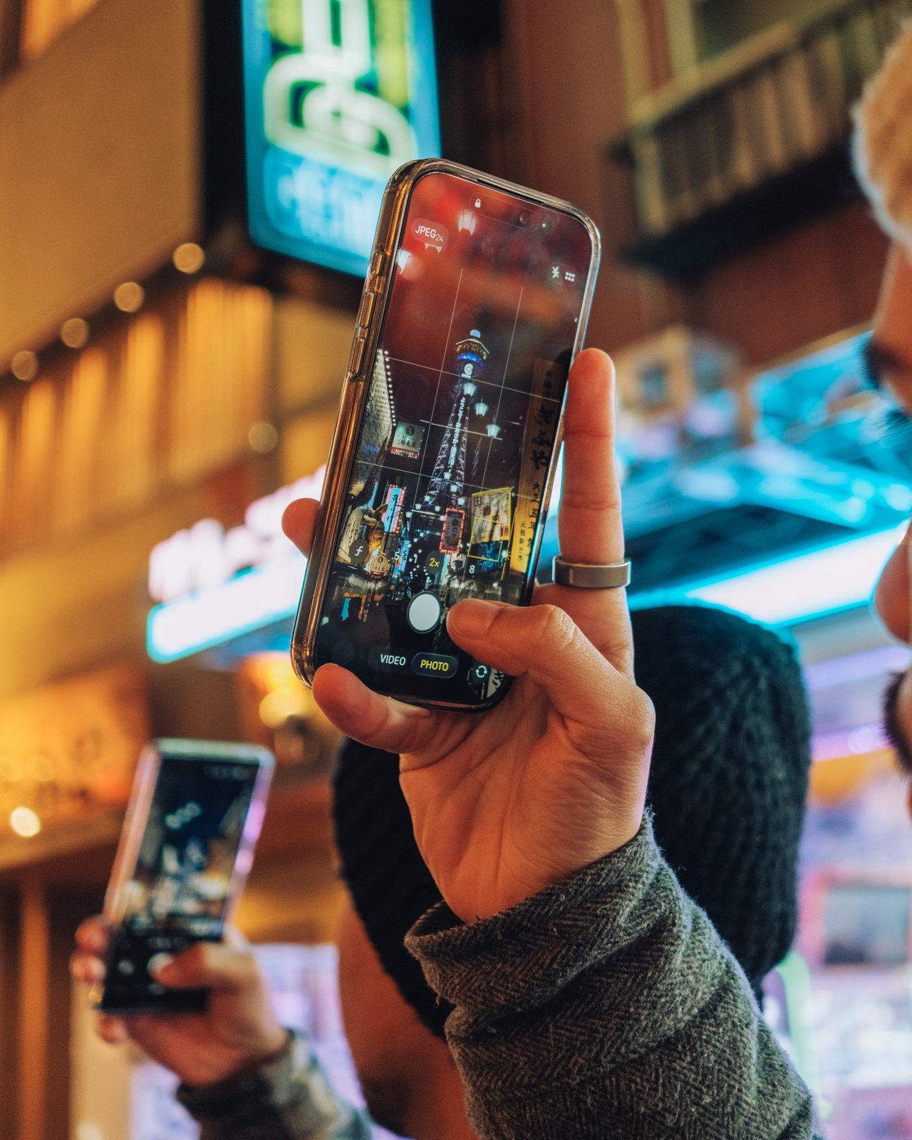 A hand holding up a phone to photograph the neon street at night, Osaka