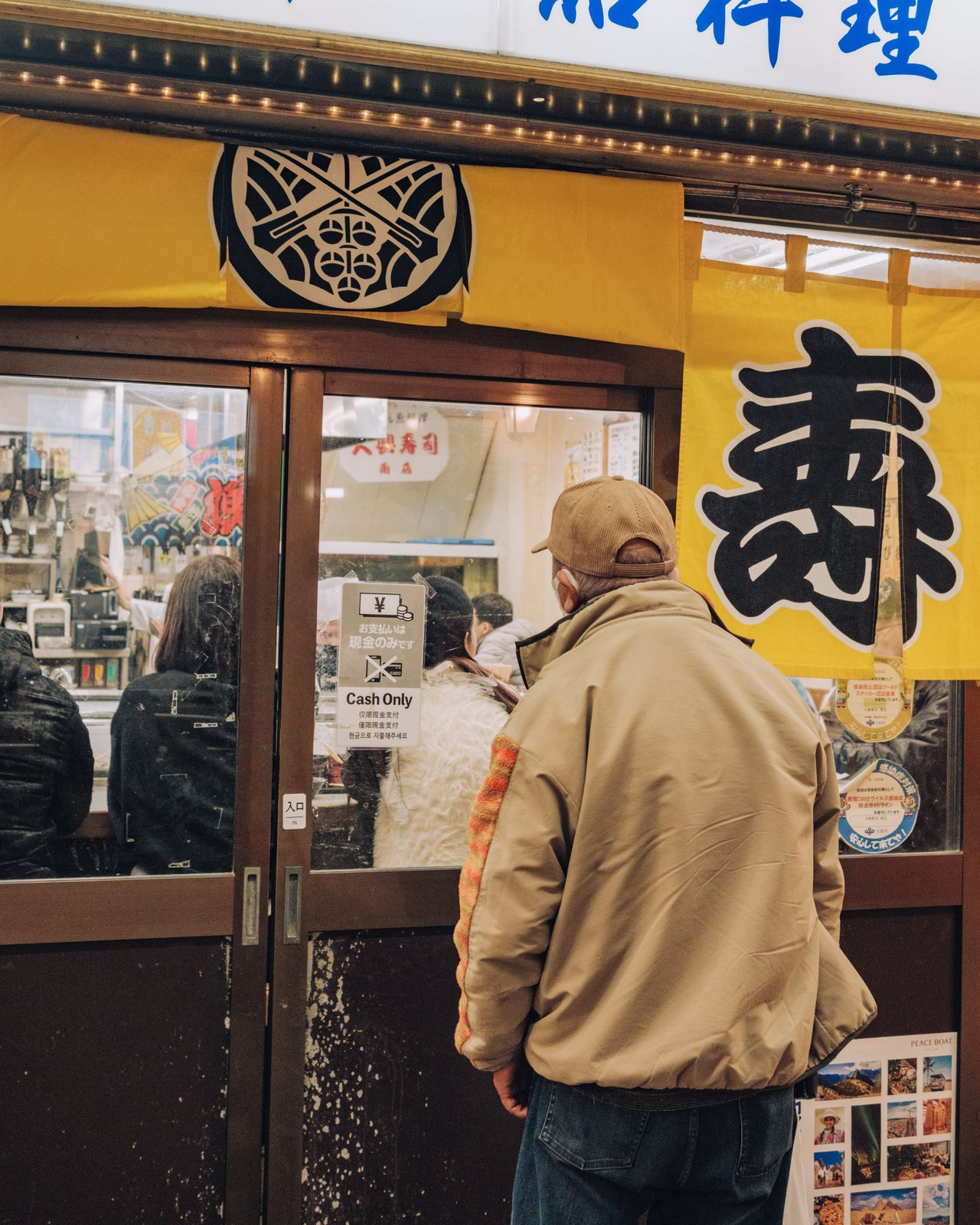 A man reading the menu outside a cash-only sushi restaurant at night, Osaka