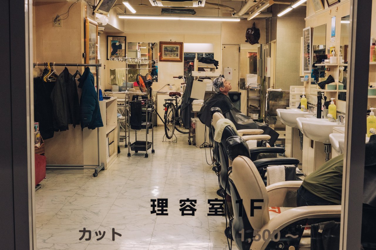 A traditional barbershop interior with barber chairs and a customer, Osaka