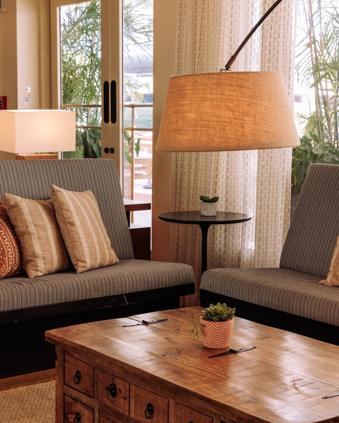 A lounge with striped sofas, an arc lamp and a wood coffee table by tall windows, The Balfour Hotel