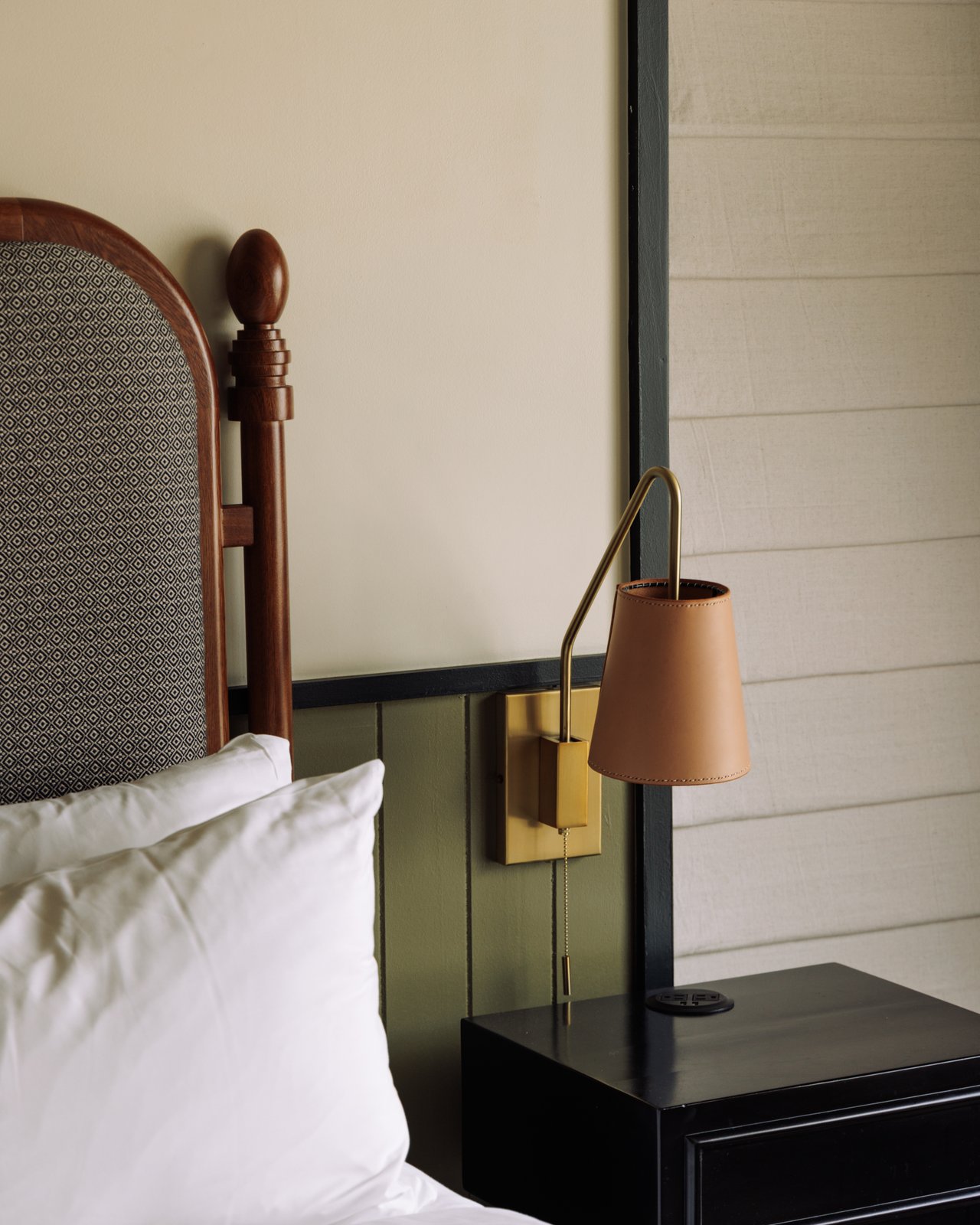 A guest-room bedside — a four-poster, a brass sconce and green wainscot, The Balfour Hotel