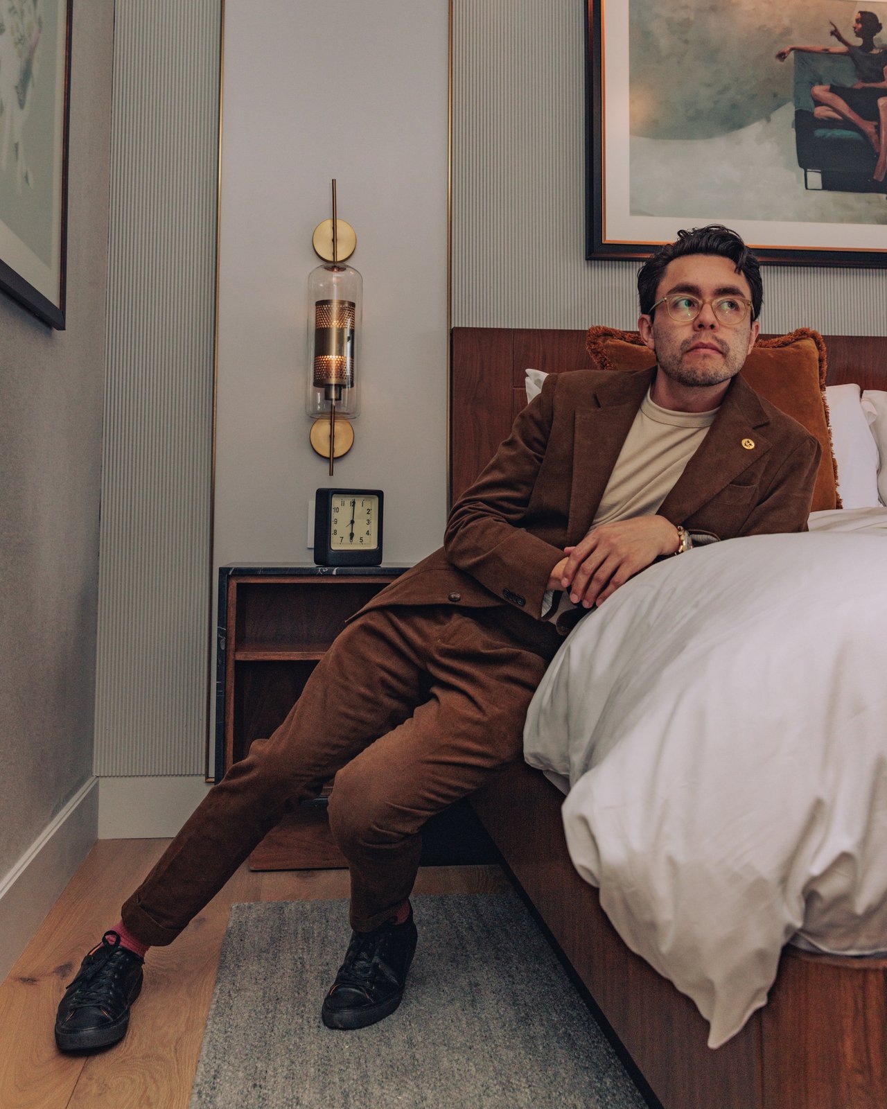 A man in a brown corduroy suit reclining against the bed in a guest room at The Global Ambassador