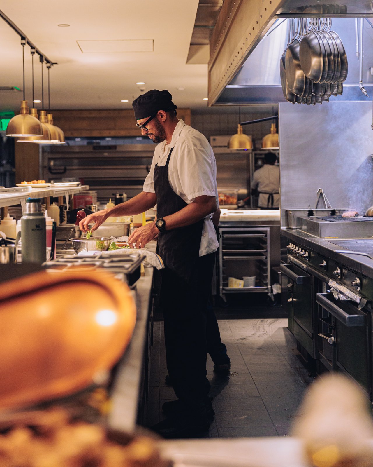 A chef plating dishes at the line of the open kitchen, copper pans overhead