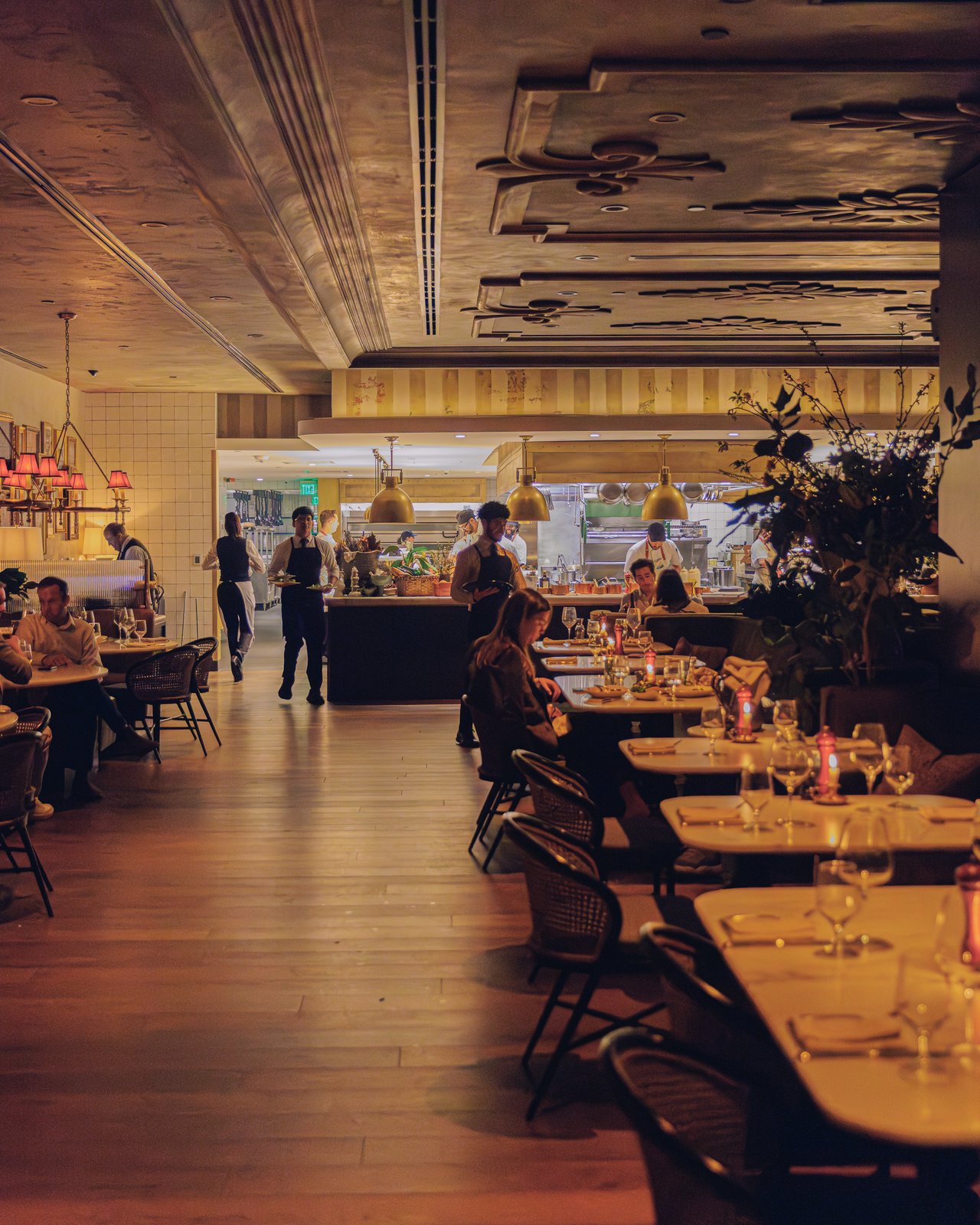 The restaurant's long communal tables set for service, diners and the open kitchen beyond