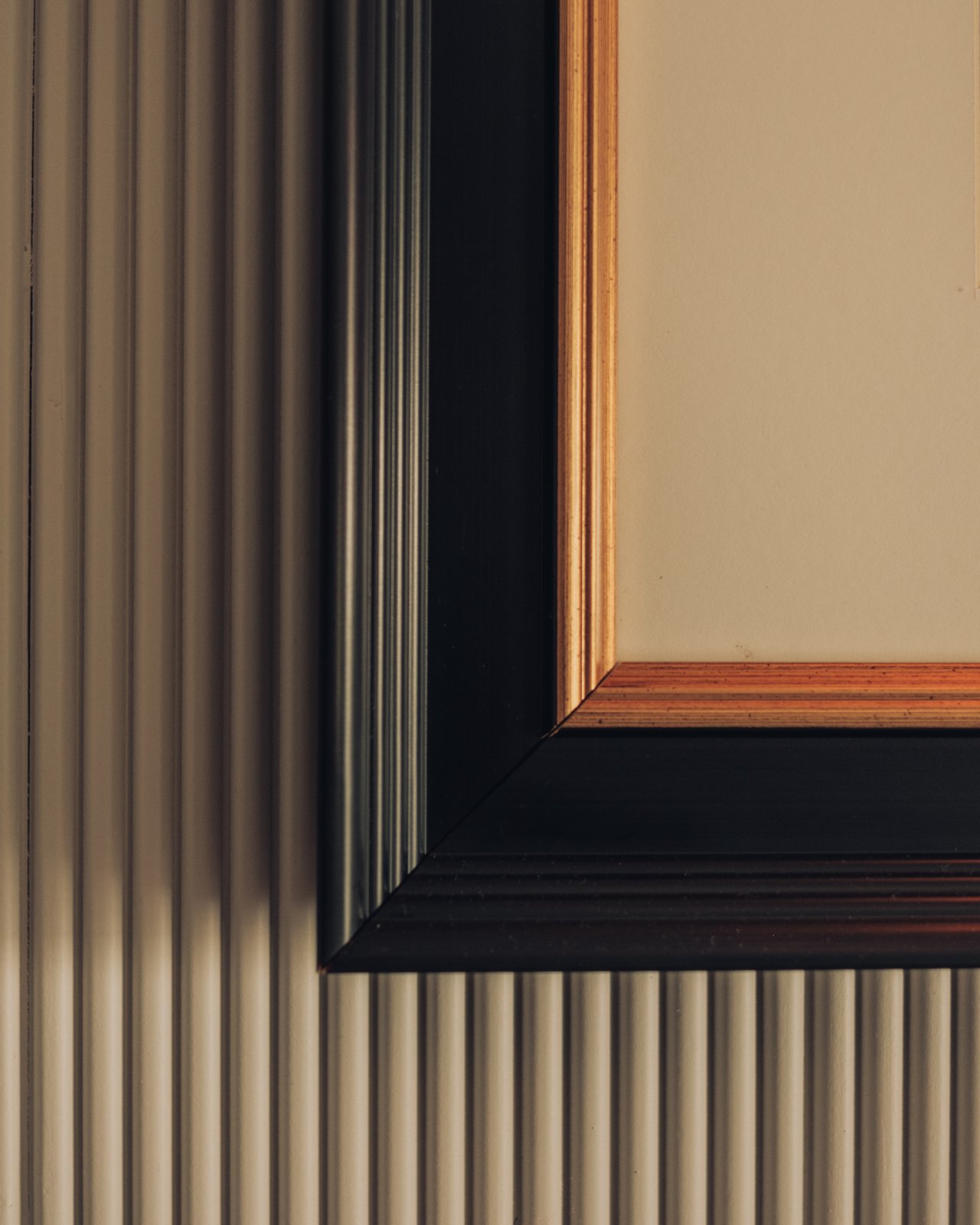 A framed mirror against a reeded wood wall, a quiet detail of a guest room