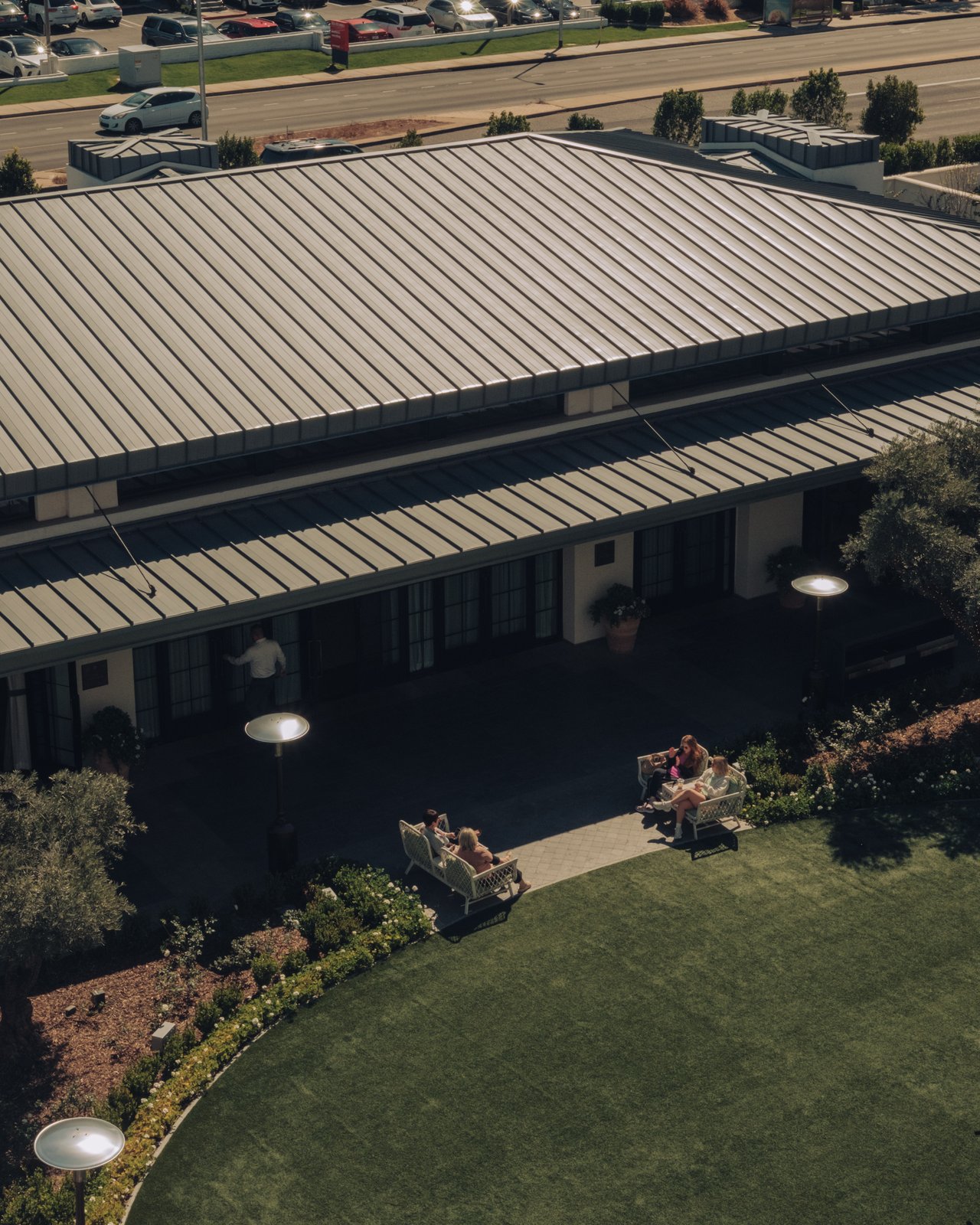 An aerial of the hotel's standing-seam metal roof and green lawn beside the freeway