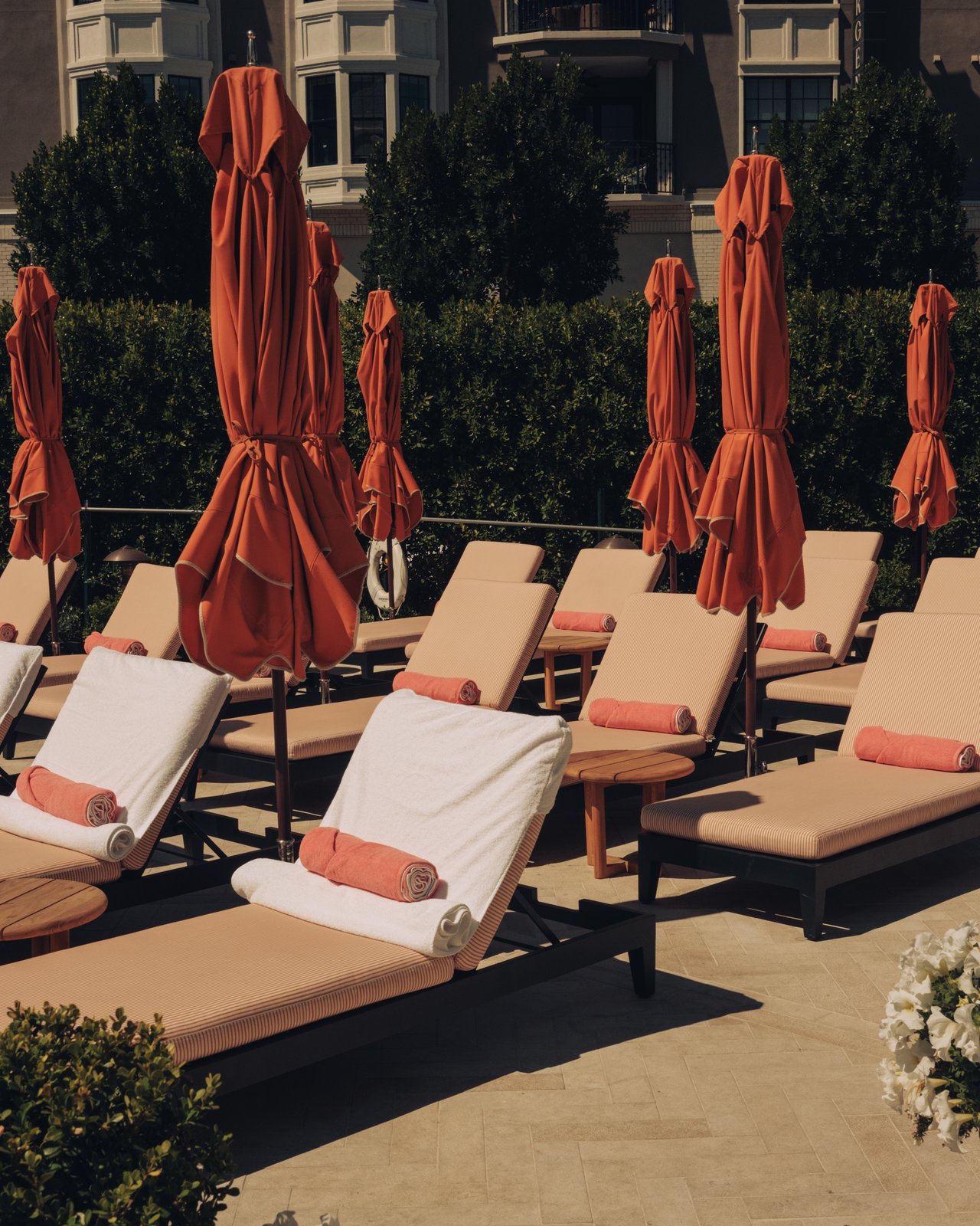Poolside chaise lounges with rolled towels and furled orange umbrellas