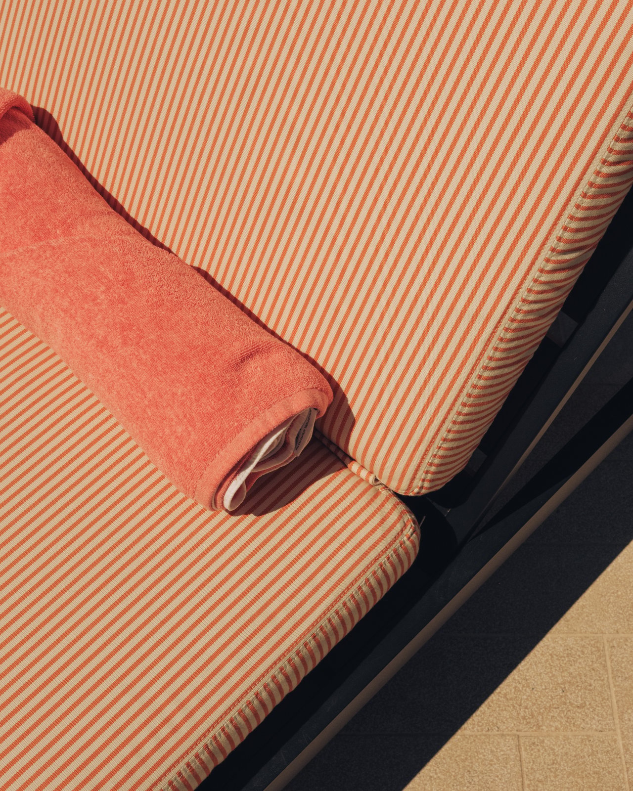 A detail of an orange-striped chaise cushion and bolster by the pool