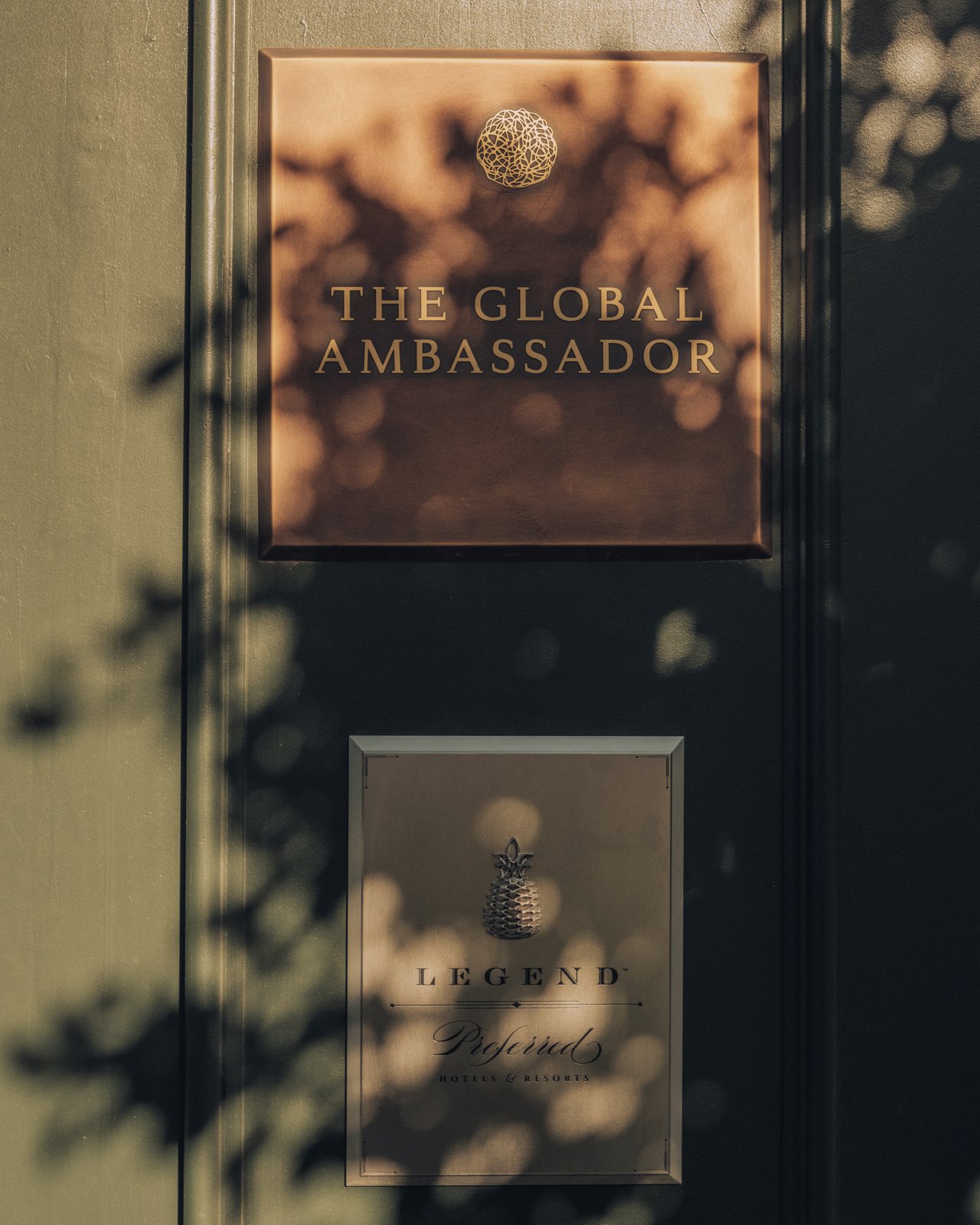 The brass 'The Global Ambassador' wall plaque in dappled shade