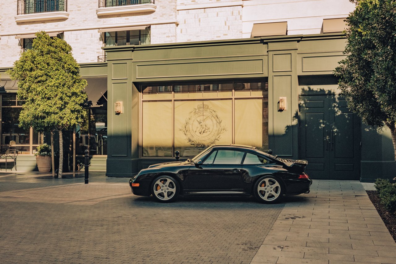 A black Porsche 911 parked at the hotel's green, crested facade