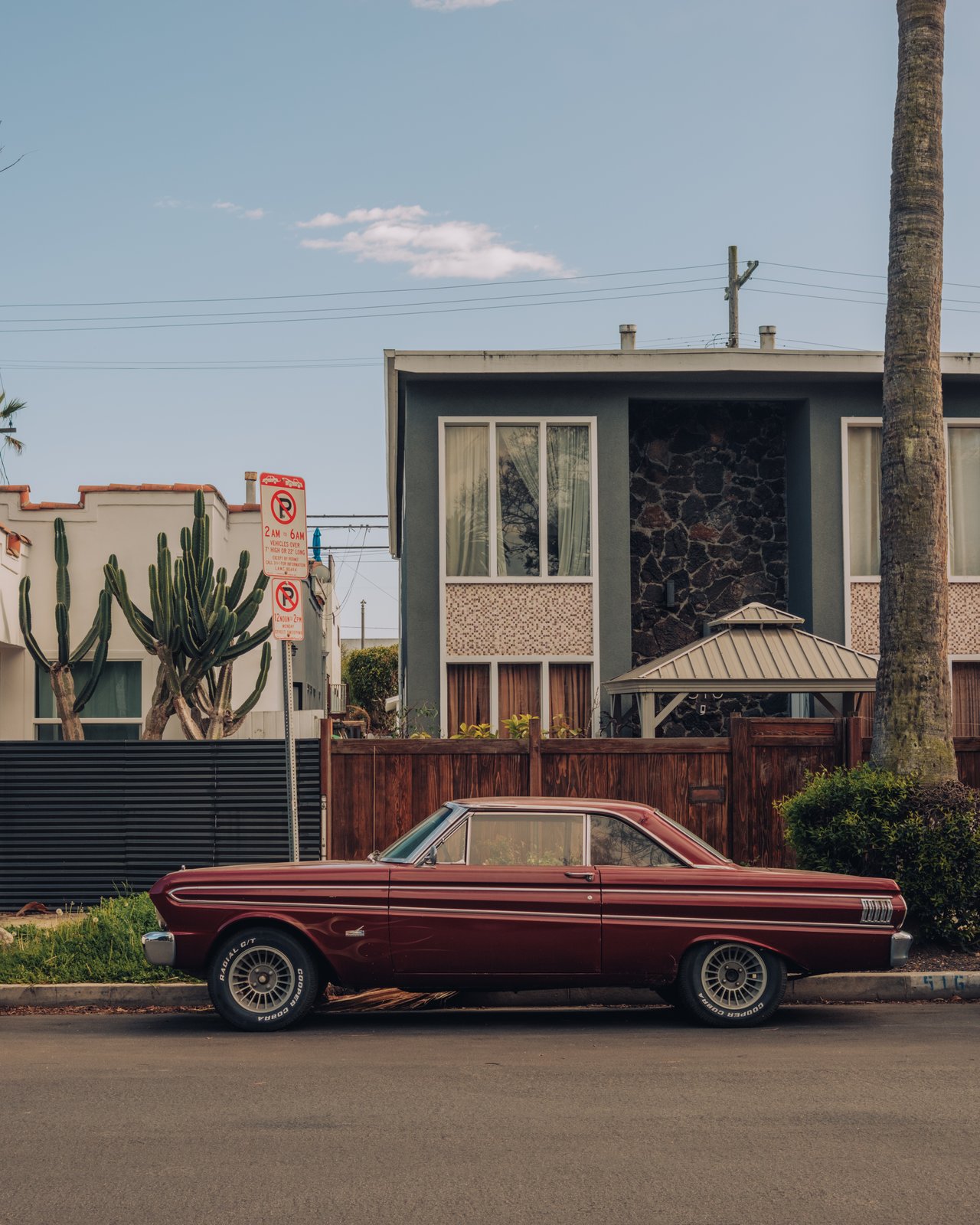 A maroon vintage Ford Falcon parked before a mid-century house with cacti, Venice