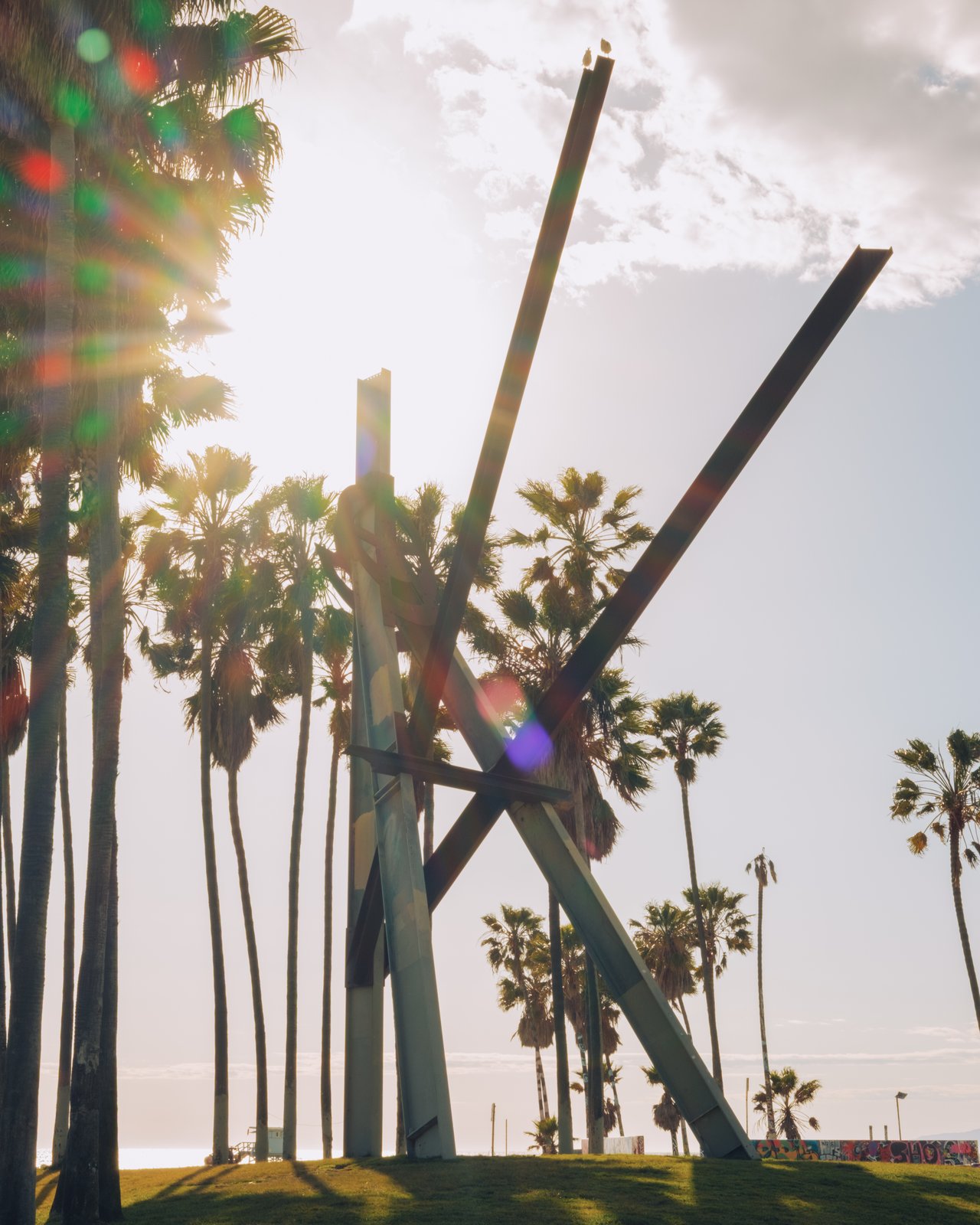 The Venice Beach kinetic steel sculpture against the sun and palms