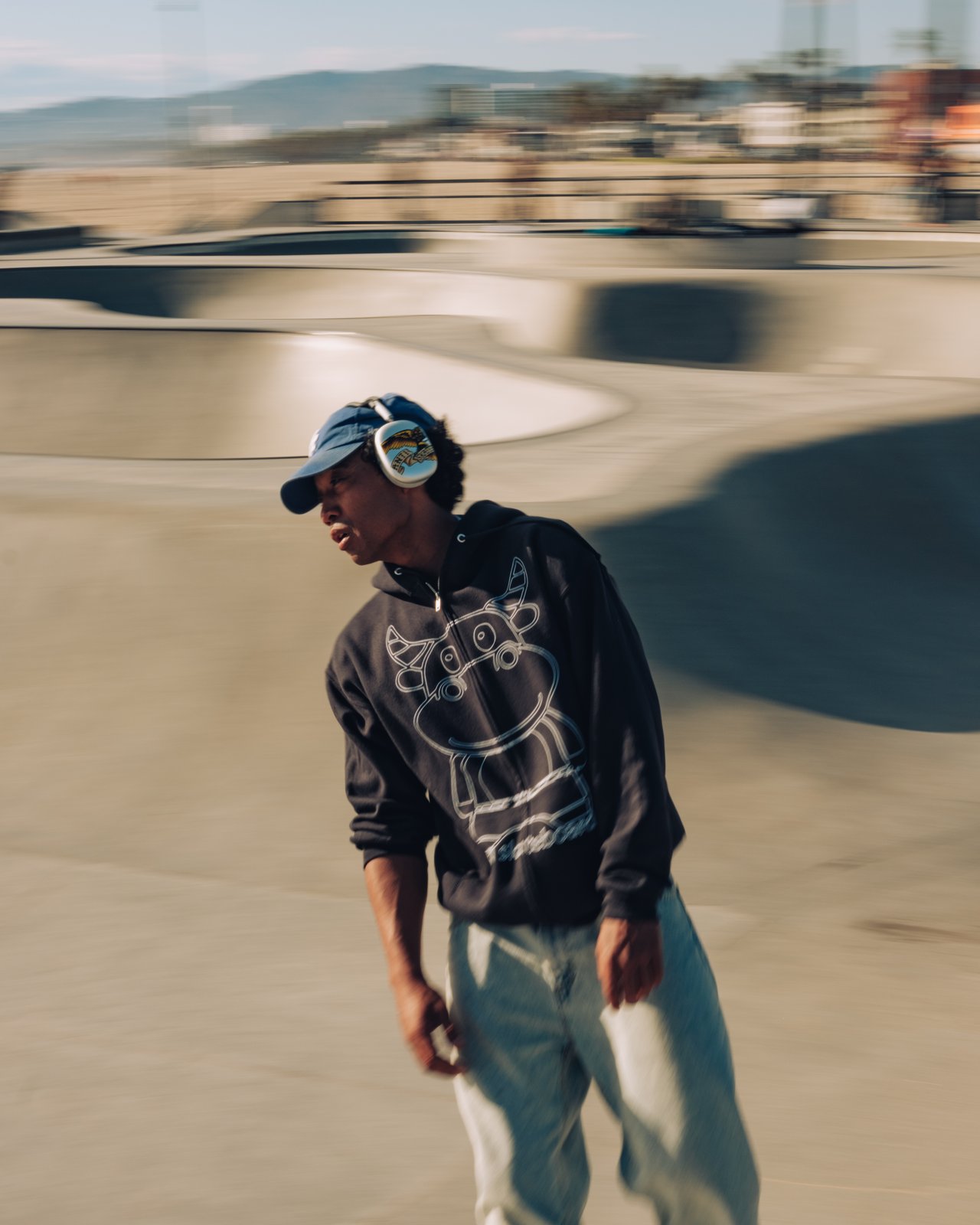 A young man in headphones and a hoodie at the Venice skate park