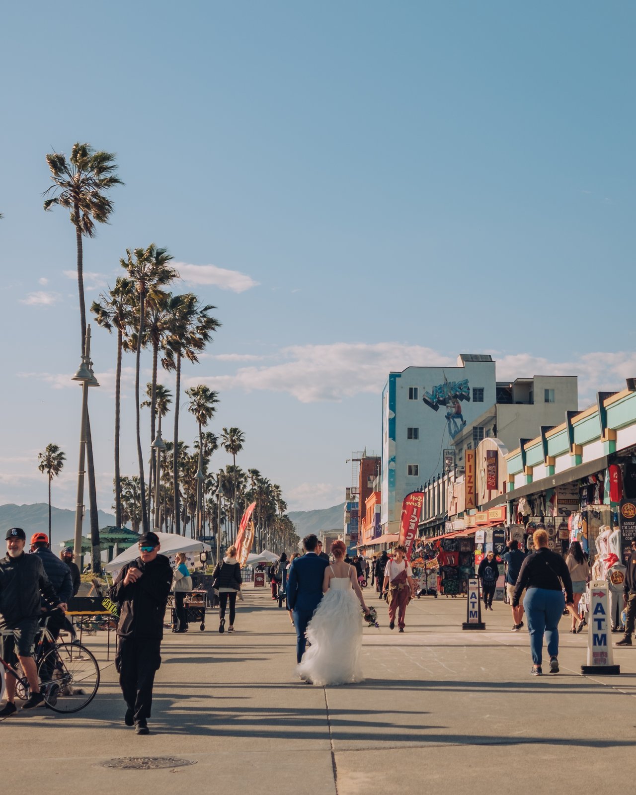 The Venice boardwalk crowd at golden hour, a bride in white among the tourists