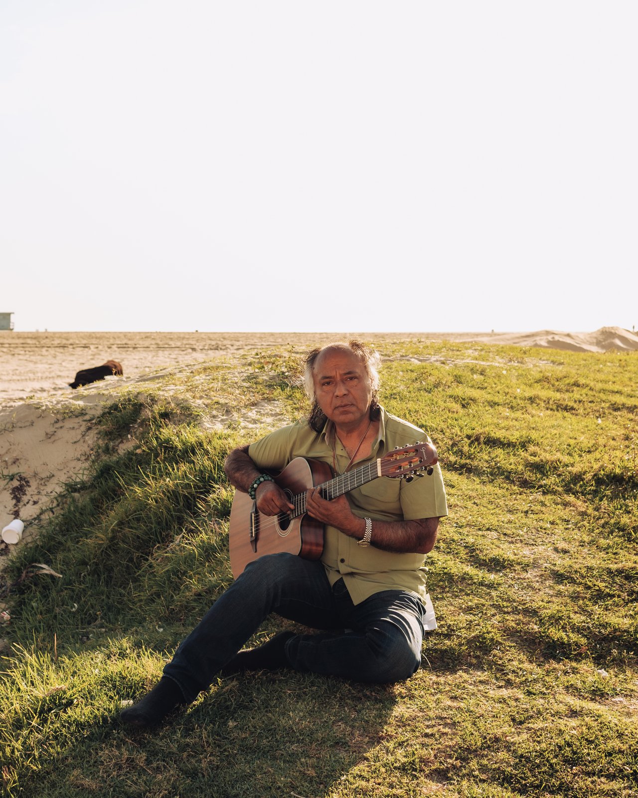 A man playing guitar on a grassy dune at golden hour, Venice Beach