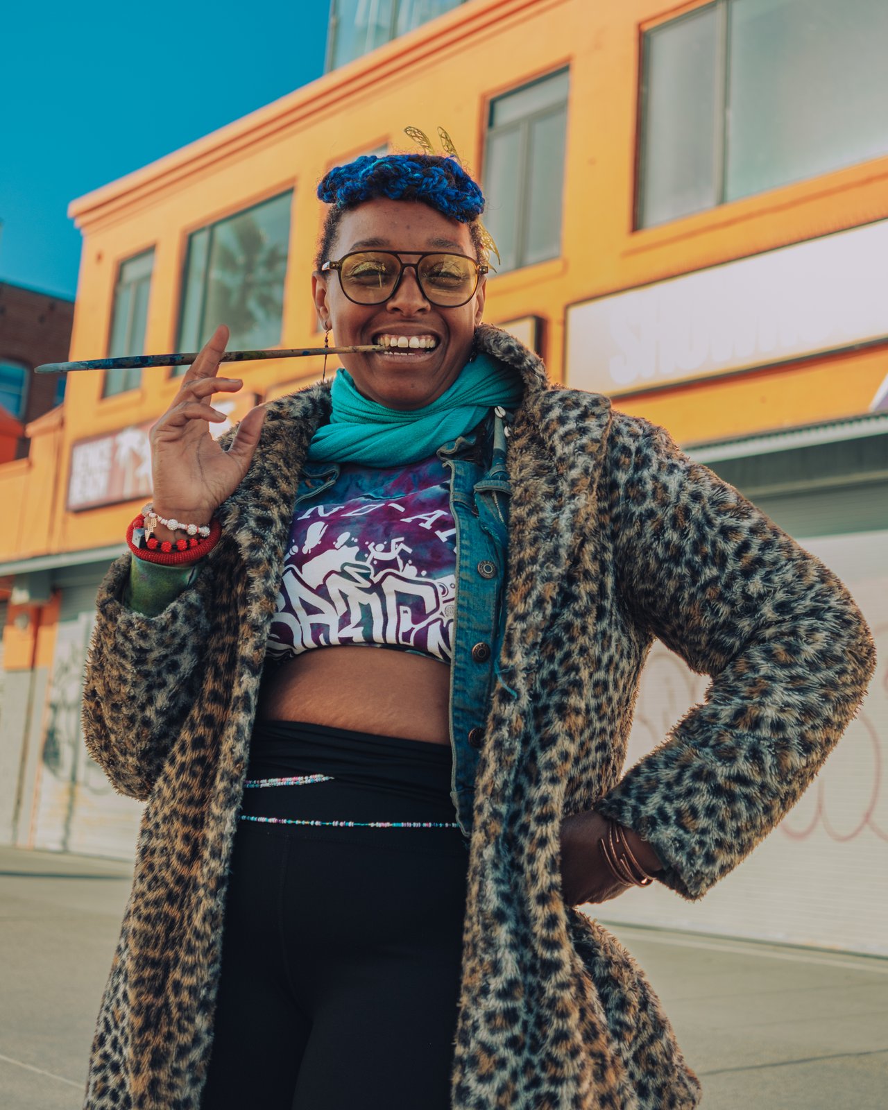 A smiling woman with blue hair and a leopard coat posing before an orange building, Venice