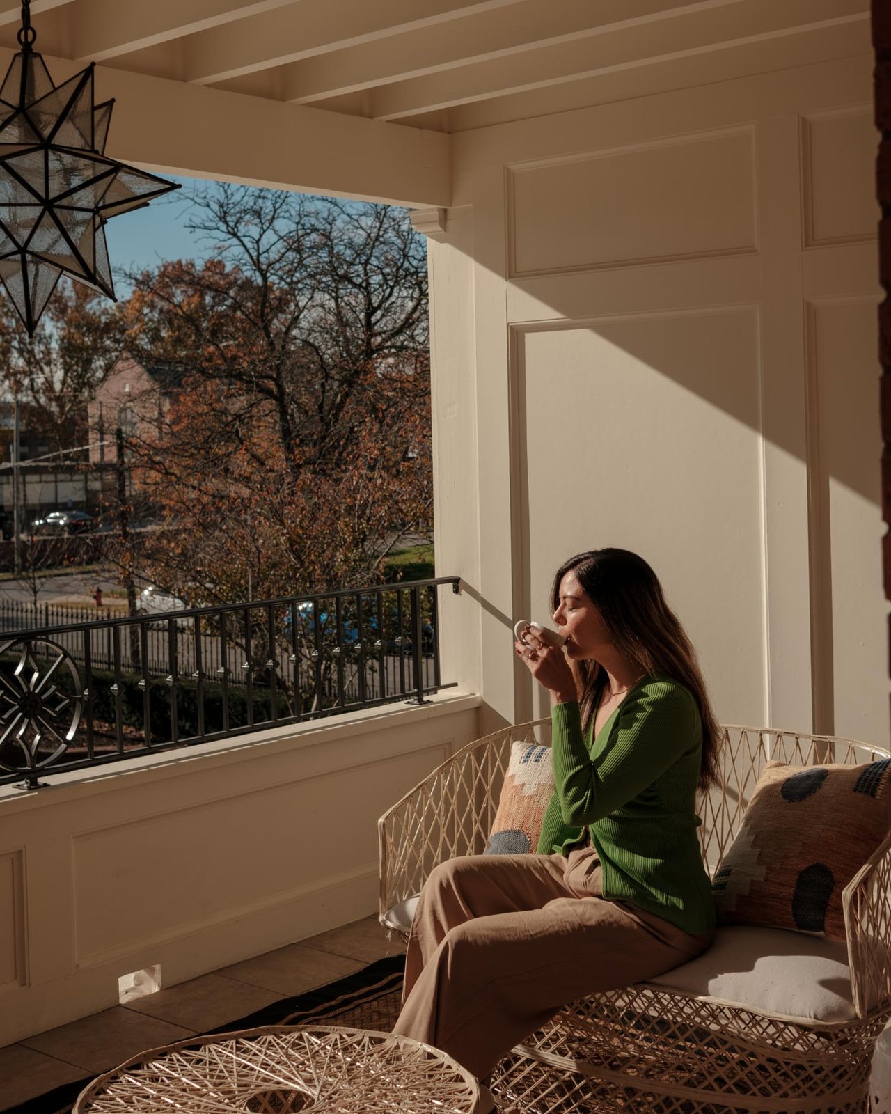 A woman sipping coffee on a rattan sofa on a sunlit porch, Kansas City