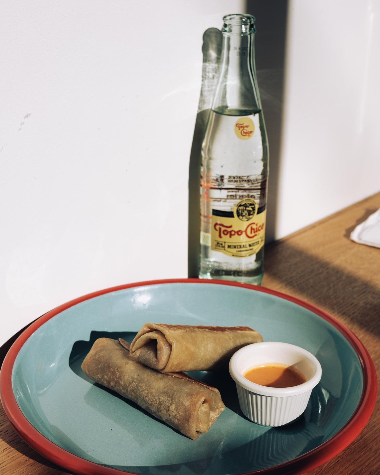 A bottle of Topo Chico beside a plate of spring rolls with dipping sauce, Kansas City