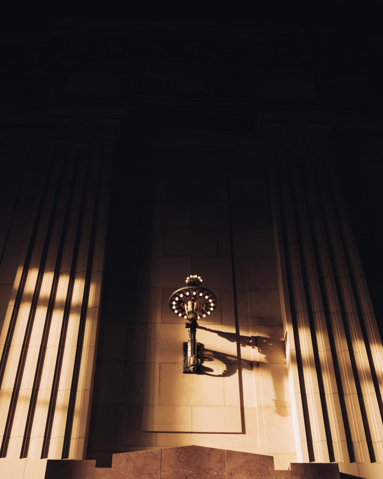 A lantern sconce casting long shadows on a fluted stone column at golden hour, Nelson-Atkins, Kansas City