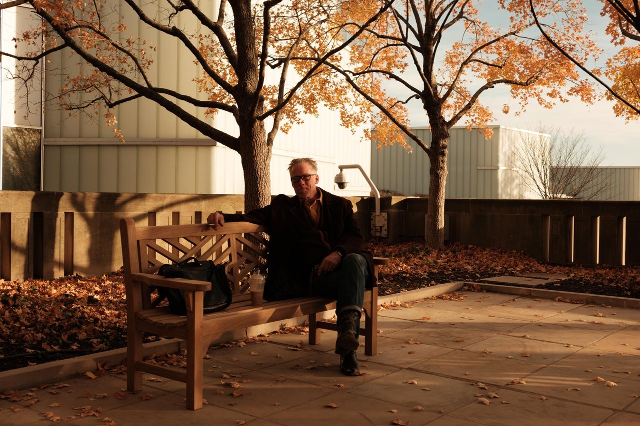 A man on a wood bench among fallen autumn leaves in the sun, Kansas City