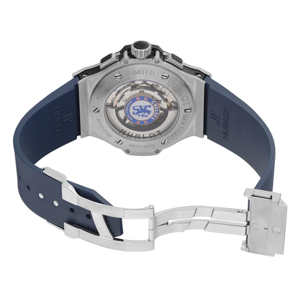An image of a pre-owned wristwatch displayed from the back view with an open clasp. The watch features a stainless steel case with visible mechanical components and a logo in the center. The angle shows the watch laying flat, with the blue rubber strap extending outward. The clasp is partially open, showcasing its metal construction. The photograph is taken from a medium distance, capturing the intricate design details clearly.