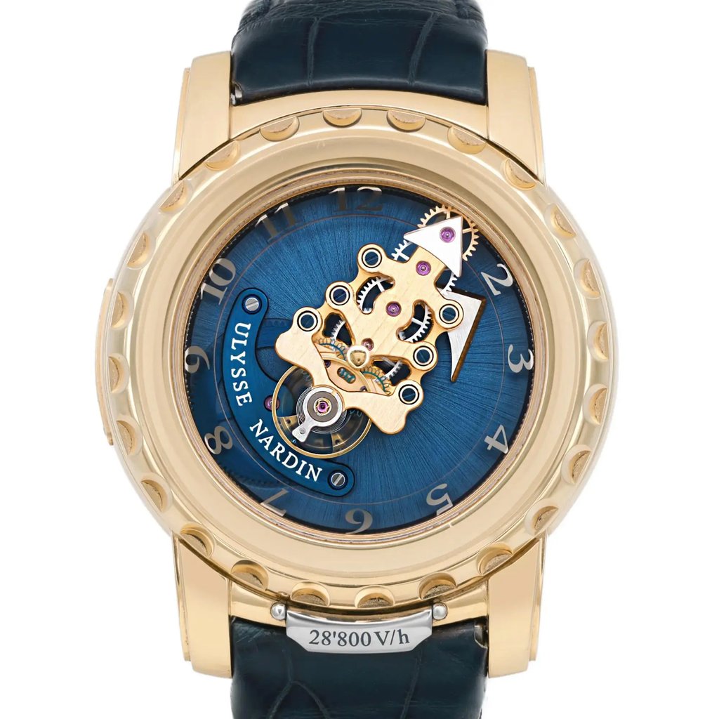 An image of a pre-owned wristwatch, captured from a front close-up angle, showcasing the watch face prominently. The watch features a gold-toned case with intricate gear mechanisms visible against a blue background. The numeral markers are elegantly displayed around the edge of the face, and a dark leather strap is partially visible at the top and bottom.