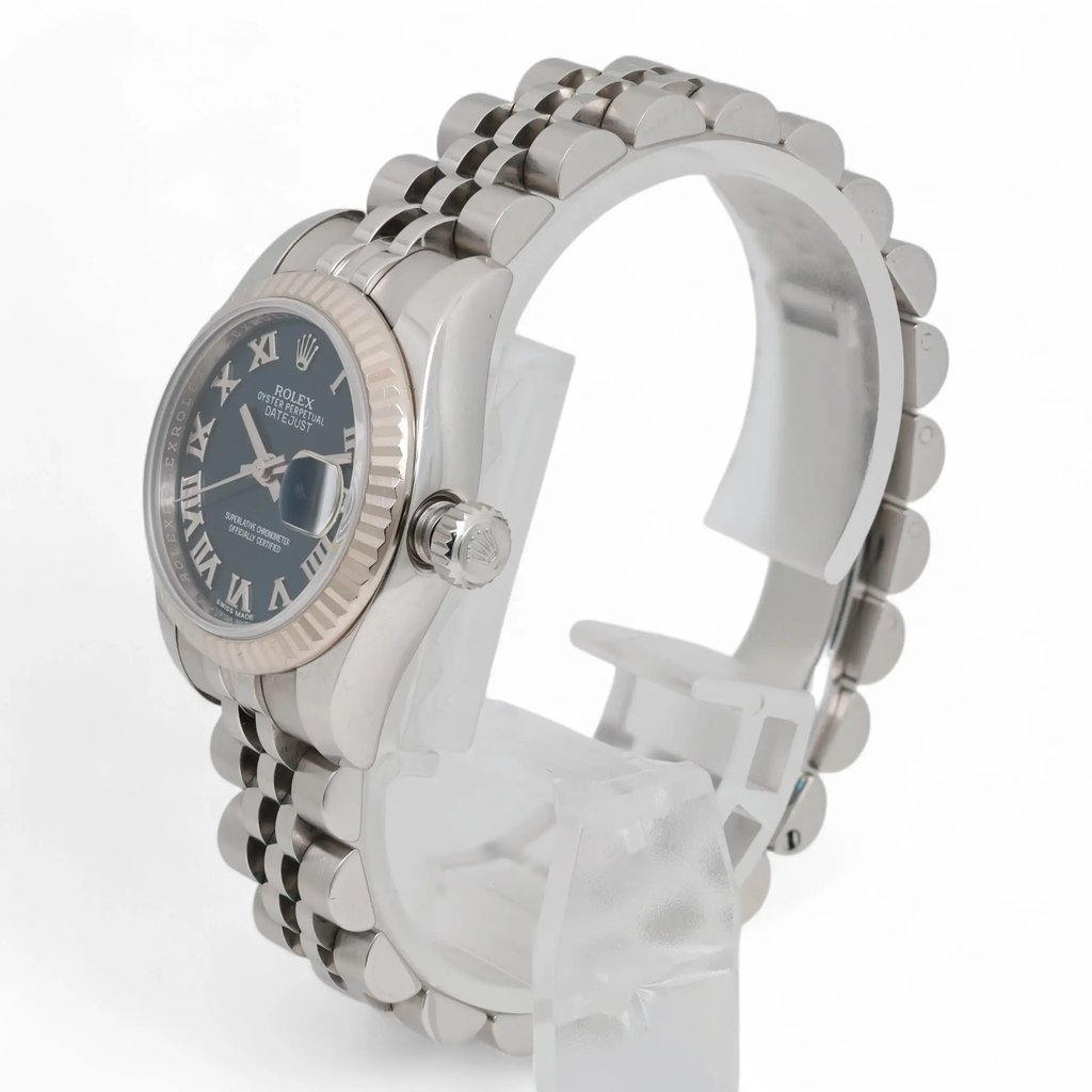 An image of a pre-owned women's Rolex wristwatch, viewed from a slightly angled side position. The watch is positioned close-up, highlighting its luminous hands and the detailed design of the Roman numeral dial. The stainless steel band is partially visible, emphasizing its polished finish.
