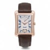 An image of a pre-owned men's Piaget Emperador Date Retrograde 18K Rose Gold Silver Dial Watch P10109 positioned upright, facing forward. The watch features a rectangular rose gold case with blue numerals on a silver dial. It has a brown leather strap and a date display at the bottom. The image is taken from a straight-on angle at a close distance, highlighting the watch's elegant design and details.