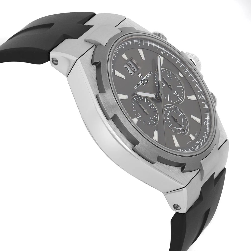 An image of a Vacheron Constantin men's wristwatch, viewed from an angled side profile. The pre-owned timepiece features a sleek black strap and a sophisticated grey dial with luminous hands and a date indicator. The watch is positioned at a slight angle, showcasing its silver-toned case and intricate details from a close distance.