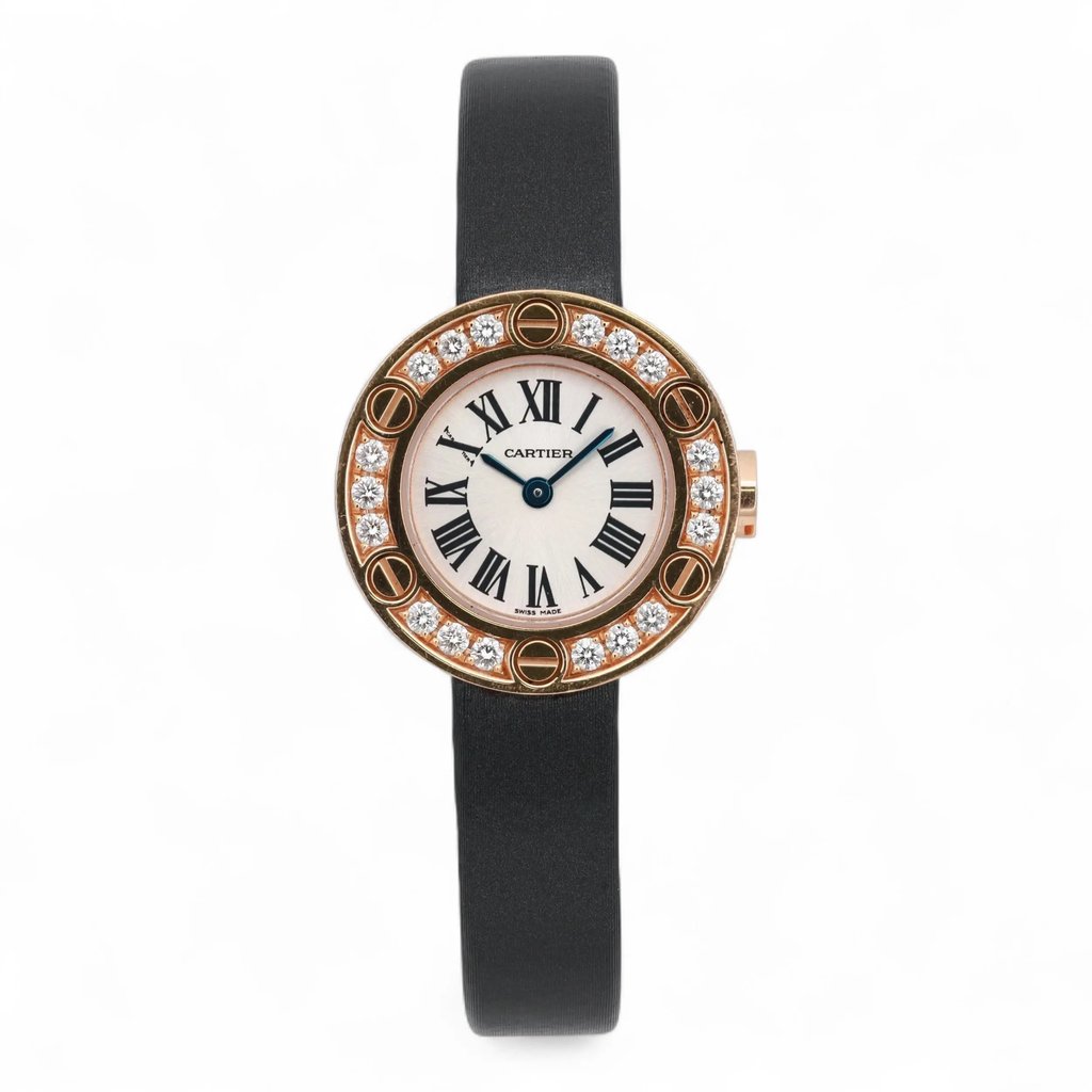 An image of a pre-owned Cartier Love Watch 18K Rose Gold Diamond Silver Dial Watch 2977 positioned upright and facing forward. The watch features a round face with a white dial, black Roman numerals, and blue hands. The bezel is adorned with sparkling diamonds set in a rose gold frame, creating an elegant contrast with the black leather strap. The image is taken from a straight-on angle at a close distance, highlighting the watch's detailed craftsmanship.