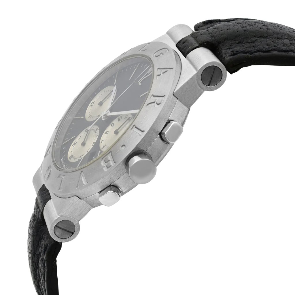 An image of a pre-owned wristwatch captured from a side profile view, highlighting the crown and pushers prominently. The watch features a metallic case with engraved markings on the bezel. The angle emphasizes the watch's thickness and details, while the black leather strap is partially visible. The photo is taken at a close distance, providing a clear view of the design and texture.
