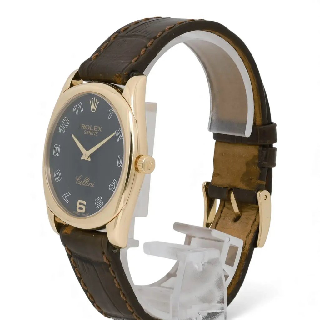 An image of a pre-owned men's Rolex wristwatch displayed at a slight angle from the front and right side. The watch features a rose gold case with a black dial, showcasing Arabic numerals and elegant watch hands. The brand name "Rolex" and "Cellini" are visible on the dial. It is positioned on a transparent stand, highlighting its brown leather strap with visible stitching. The watch is captured at a close distance, emphasizing its luxurious details.