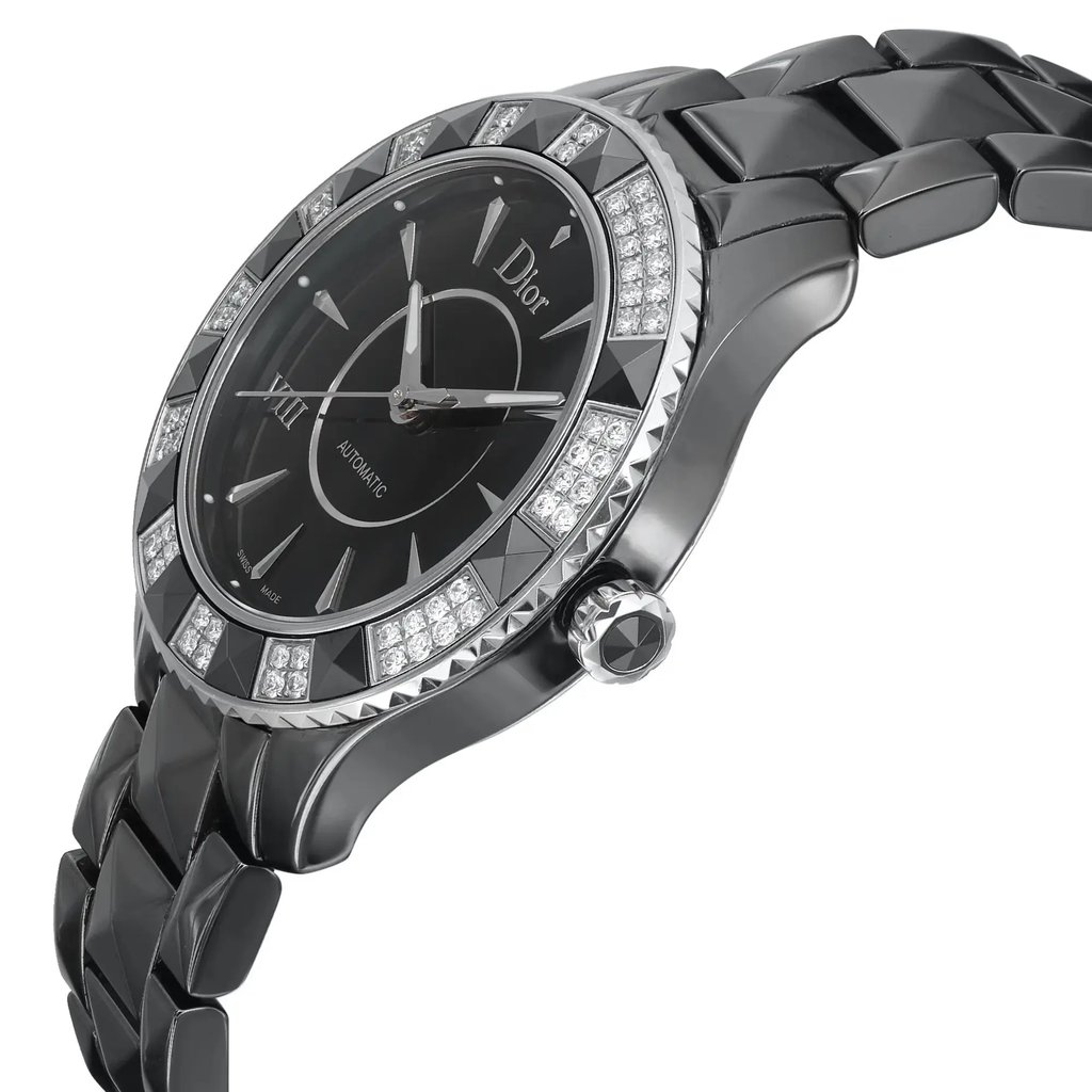 An image of a pre-owned wristwatch shown from a side profile view. The focus is on the crown, which is prominently displayed. The watch's face is angled slightly to the left, showcasing a dark dial with geometric patterns and diamond accents around the bezel. The metal bracelet is visible, adding to the elegant design. The photo is taken from a close distance, highlighting the watch's intricate details and craftsmanship.