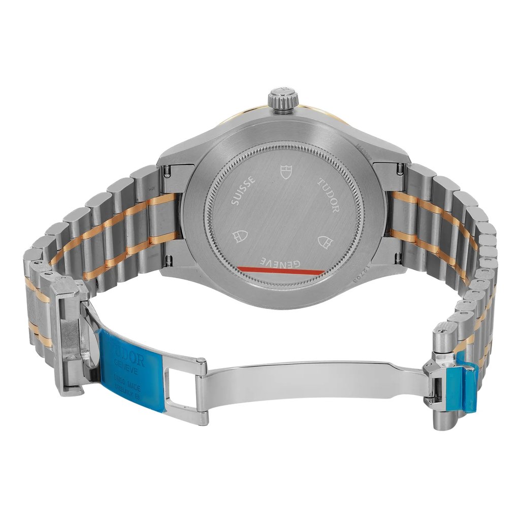 An image of a wristwatch showing the back view with an open clasp. The watch is unworn and has a stainless steel and gold-tone link bracelet. The case back displays engravings, and the clasp is partially covered with a blue protective film. The angle captures the watch from a slightly elevated perspective, providing a clear view of the bracelet and clasp details.