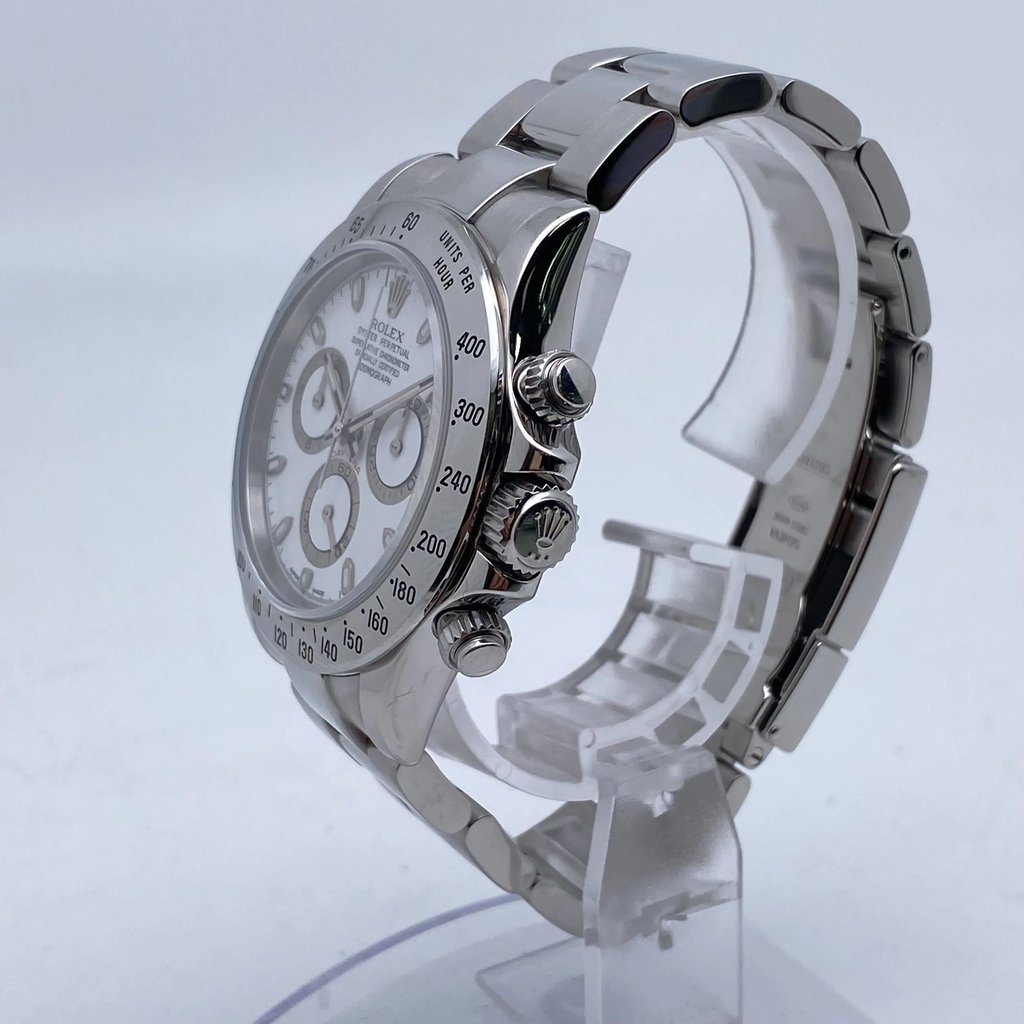 An image of a pre-owned men's Rolex wristwatch, featuring a chronograph, luminous hands, and a small seconds subdial. The watch is positioned at a slight angle, showcasing the right side with the crown and pushers clearly visible. It is mounted on a display stand, with the metal bracelet partially open. The image is taken at a close distance to highlight the details of the watch face and bezel.