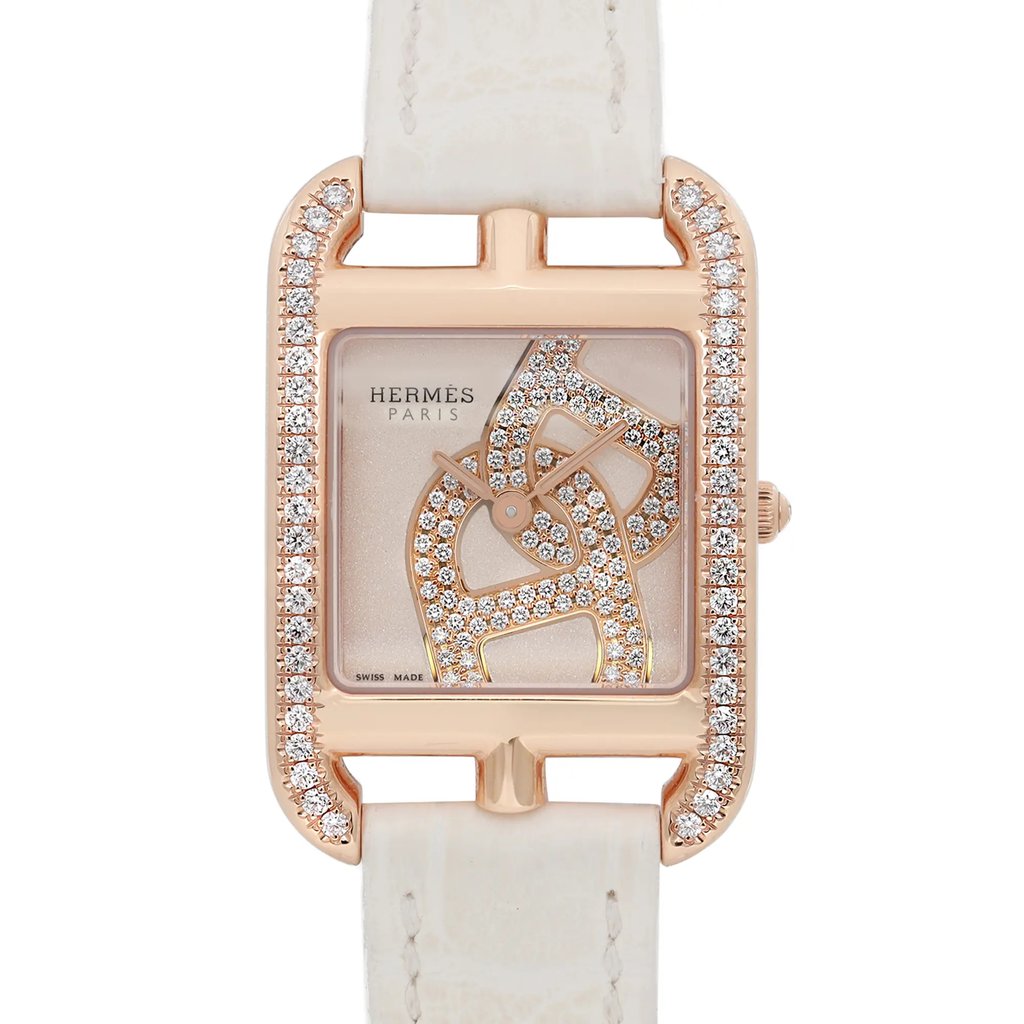 An image of a pre-owned women's HERMÈS Cod Joaillier wristwatch. The watch is positioned upright, showcasing a rectangular face adorned with intricate, diamond-studded designs. It features a 18k rose gold case with additional diamond embellishments along the edges. The watch is photographed from a front angle at a close distance, emphasizing its luxurious details and craftsmanship. The strap is light-colored, contrasting elegantly with the watch face.